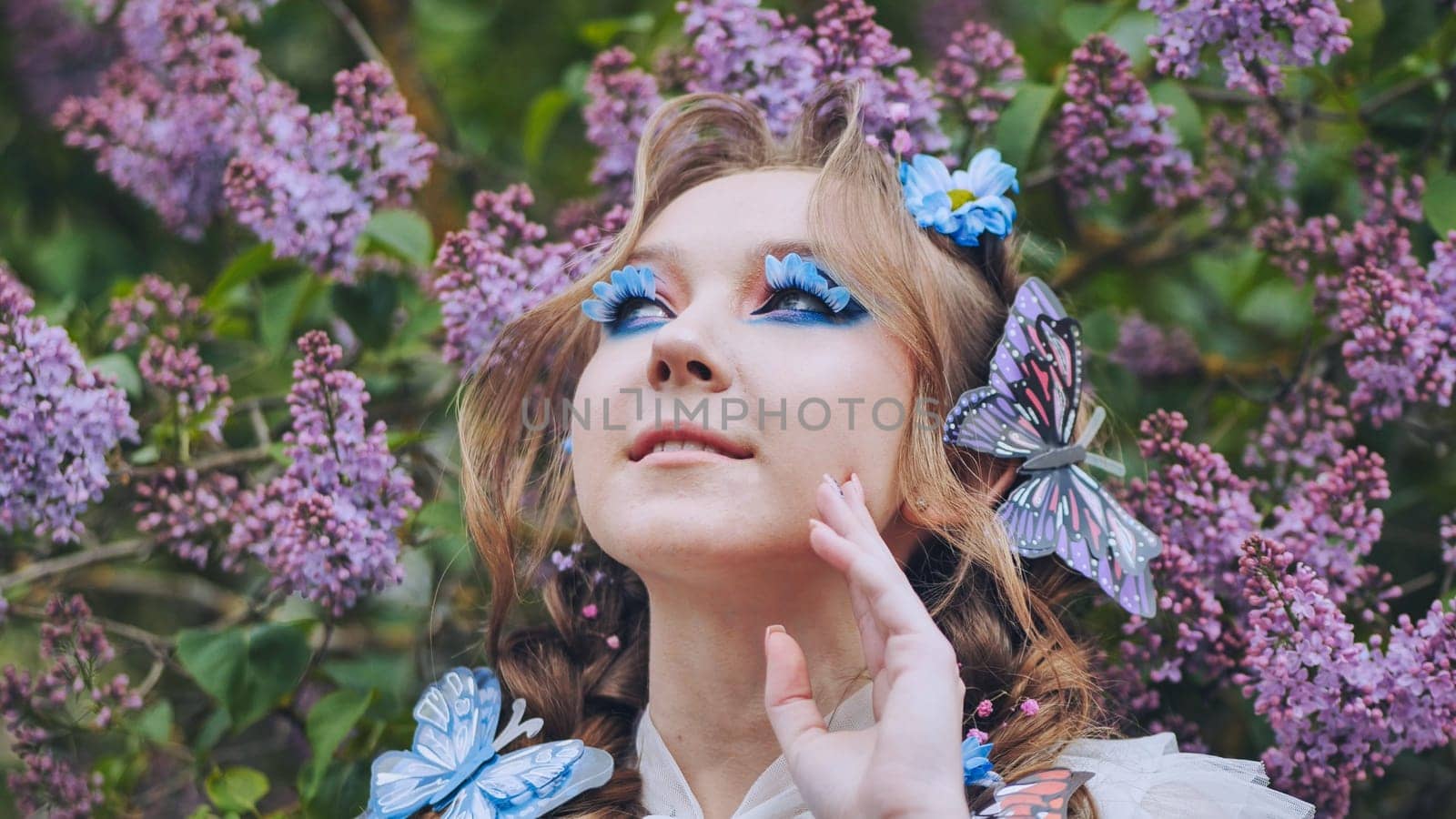 A young girl poses in lilac with a beautiful hairstyle of flowers and butterflies