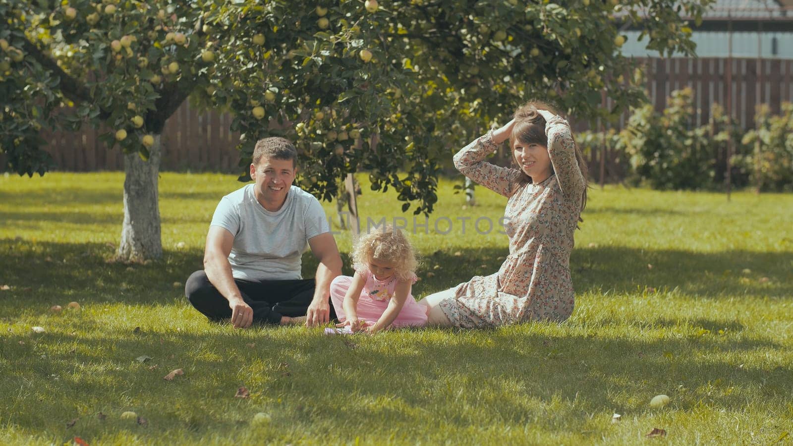 A young family on the grass in the garden outside their home. by DovidPro