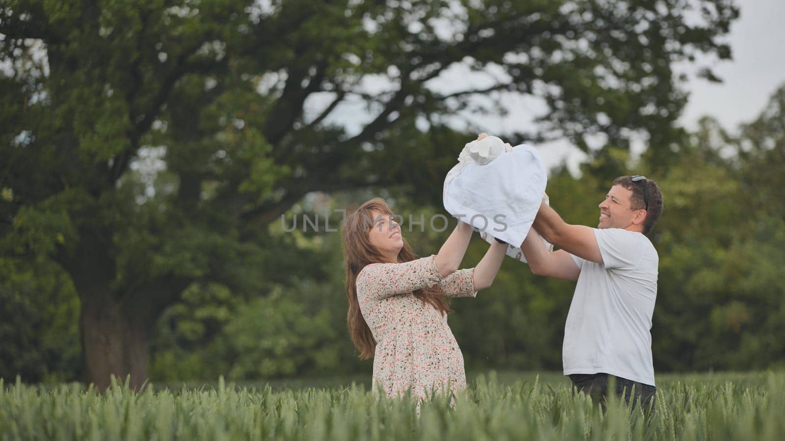 The young couple lifts their newborn baby up and kisses in a field of wheat