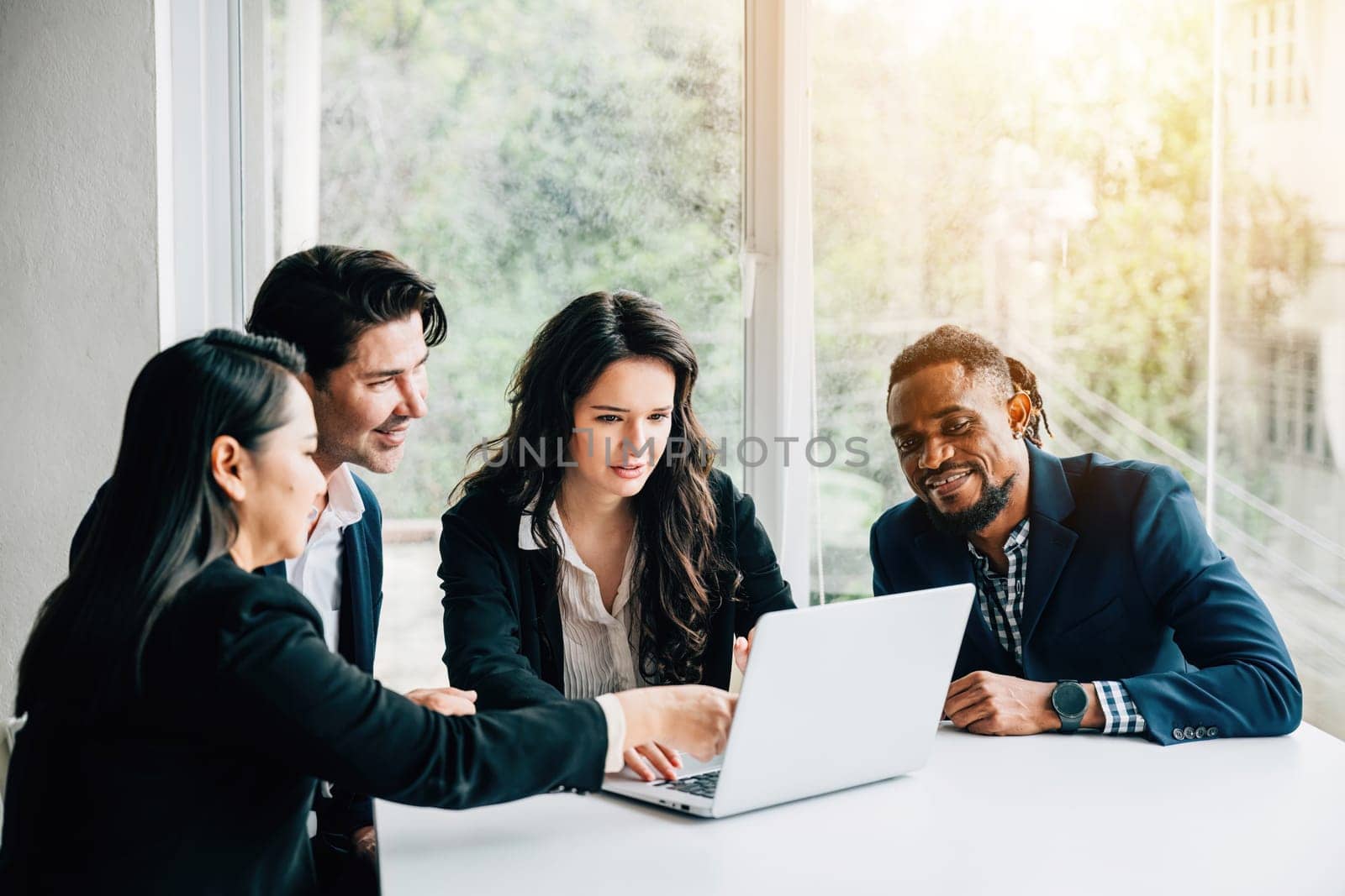 Diverse business team, including both men and women, collaborates in meeting room using laptop. Their teamwork, diversity and cooperation are evident as they discuss, plan, and strategize for success. by Sorapop