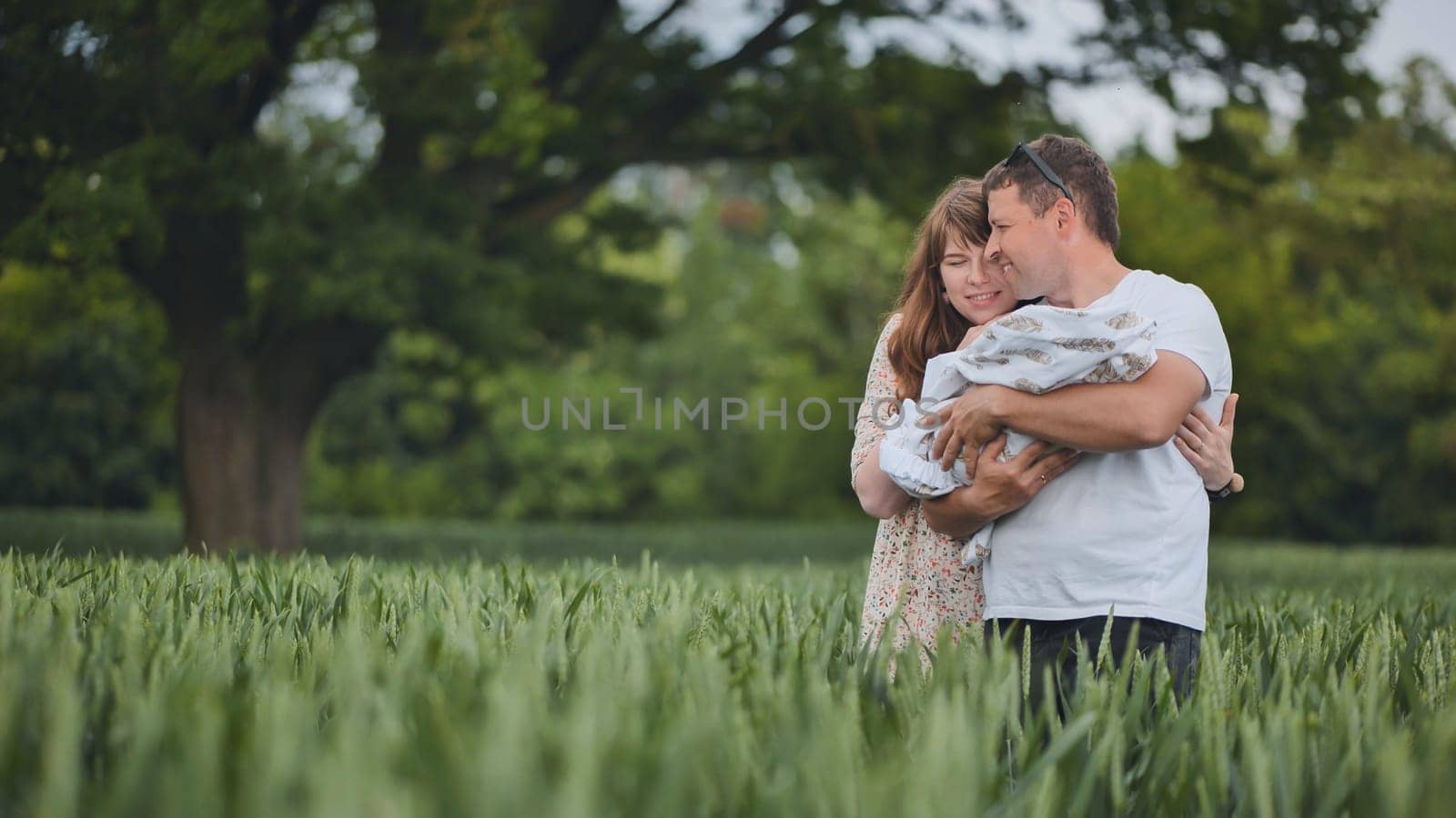 A young couple with their newborn baby in green wheat in a field
