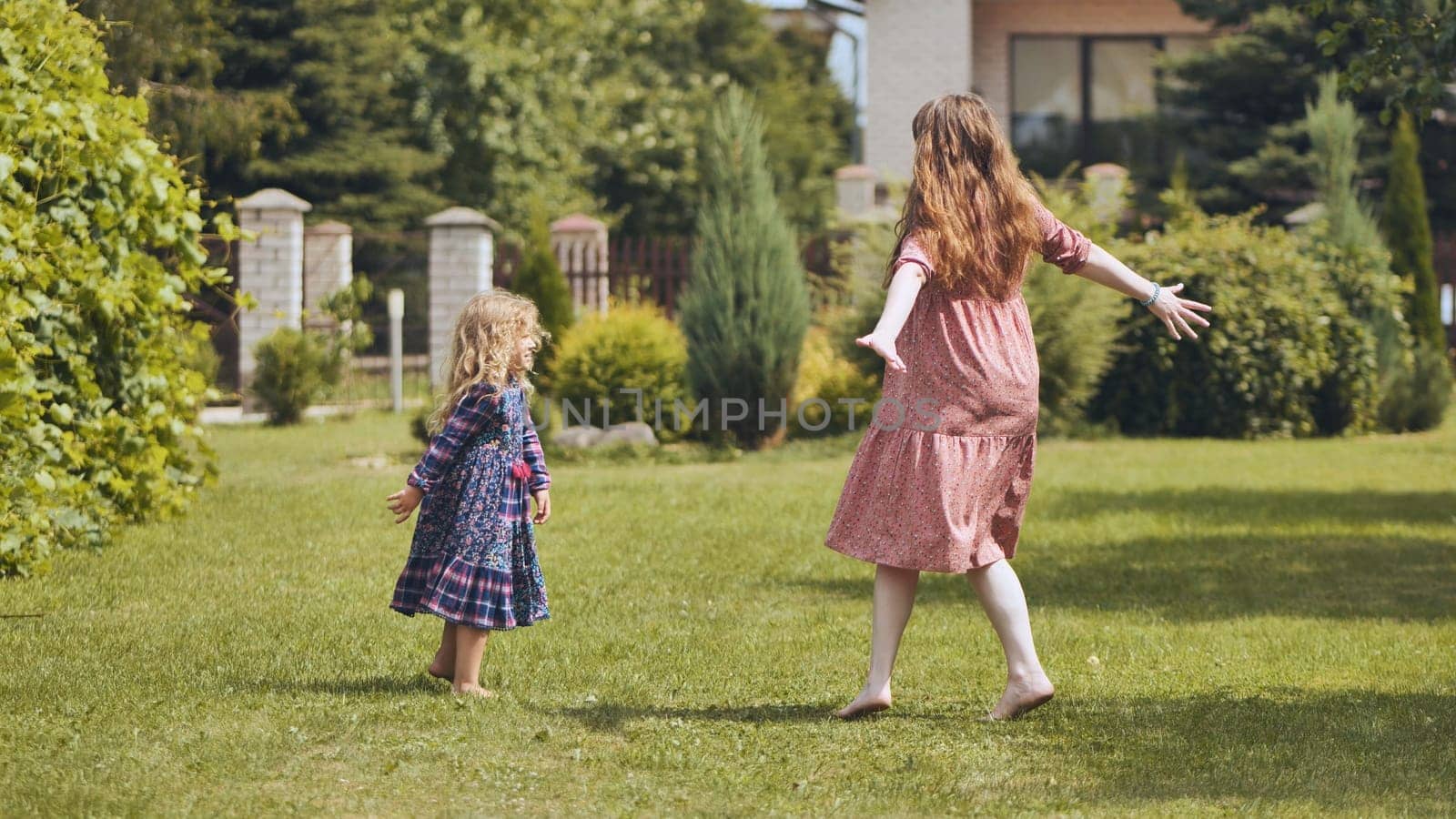 A mother and her daughter twirl in the garden outside the house. by DovidPro