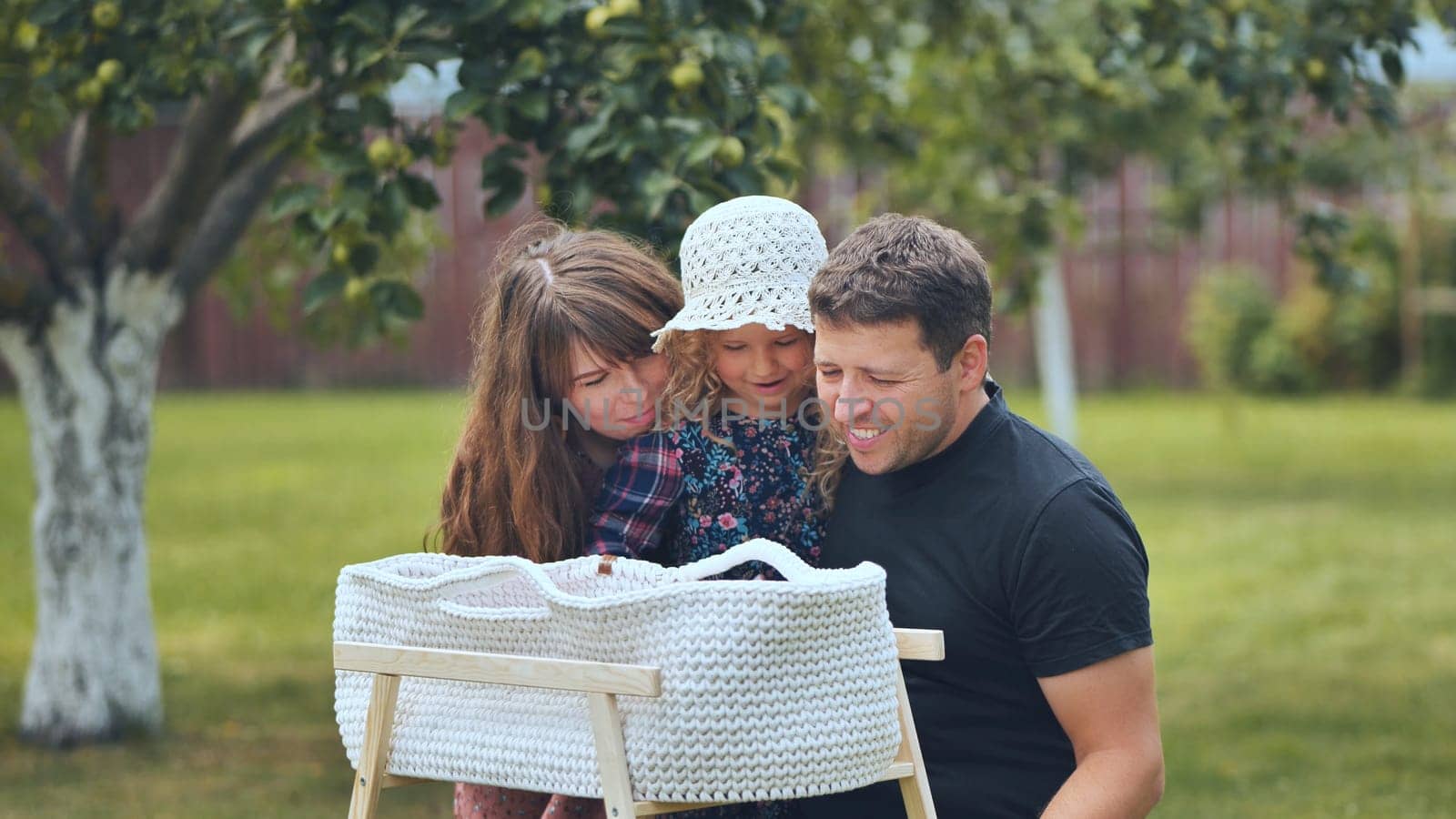 A young family looks at their newborn baby in a cradle in the garden