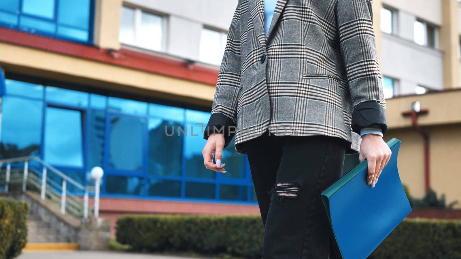 A young student girl in torn jeans and folders in her hands walks through the city