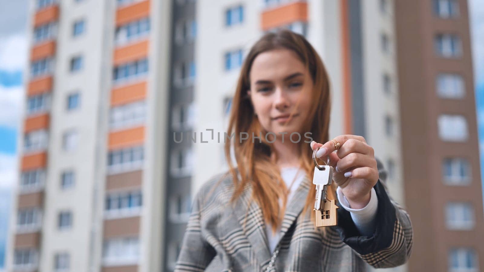 The girl shows the keys to the apartment against the backdrop of an apartment building. by DovidPro