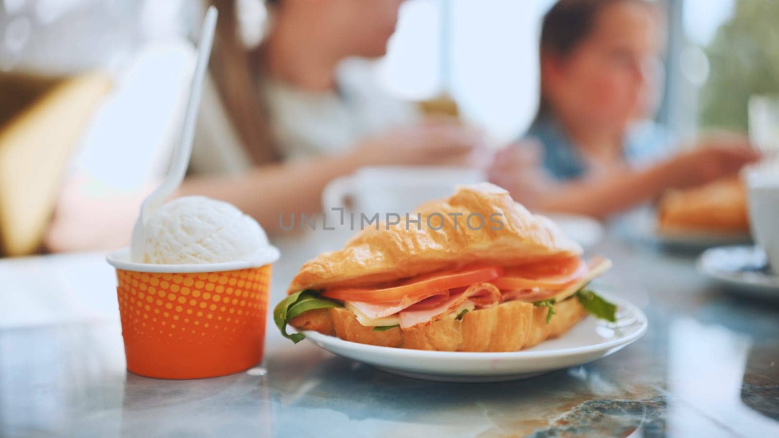 Ice cream and croissant with meat against the background of people eating in the cafe