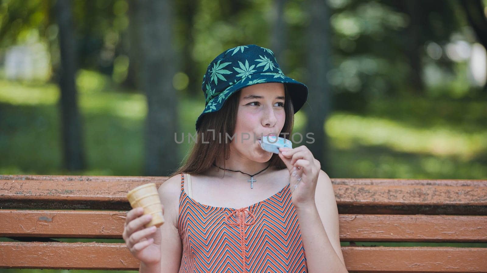 Teenage girl eating ice cream in the park on the bench