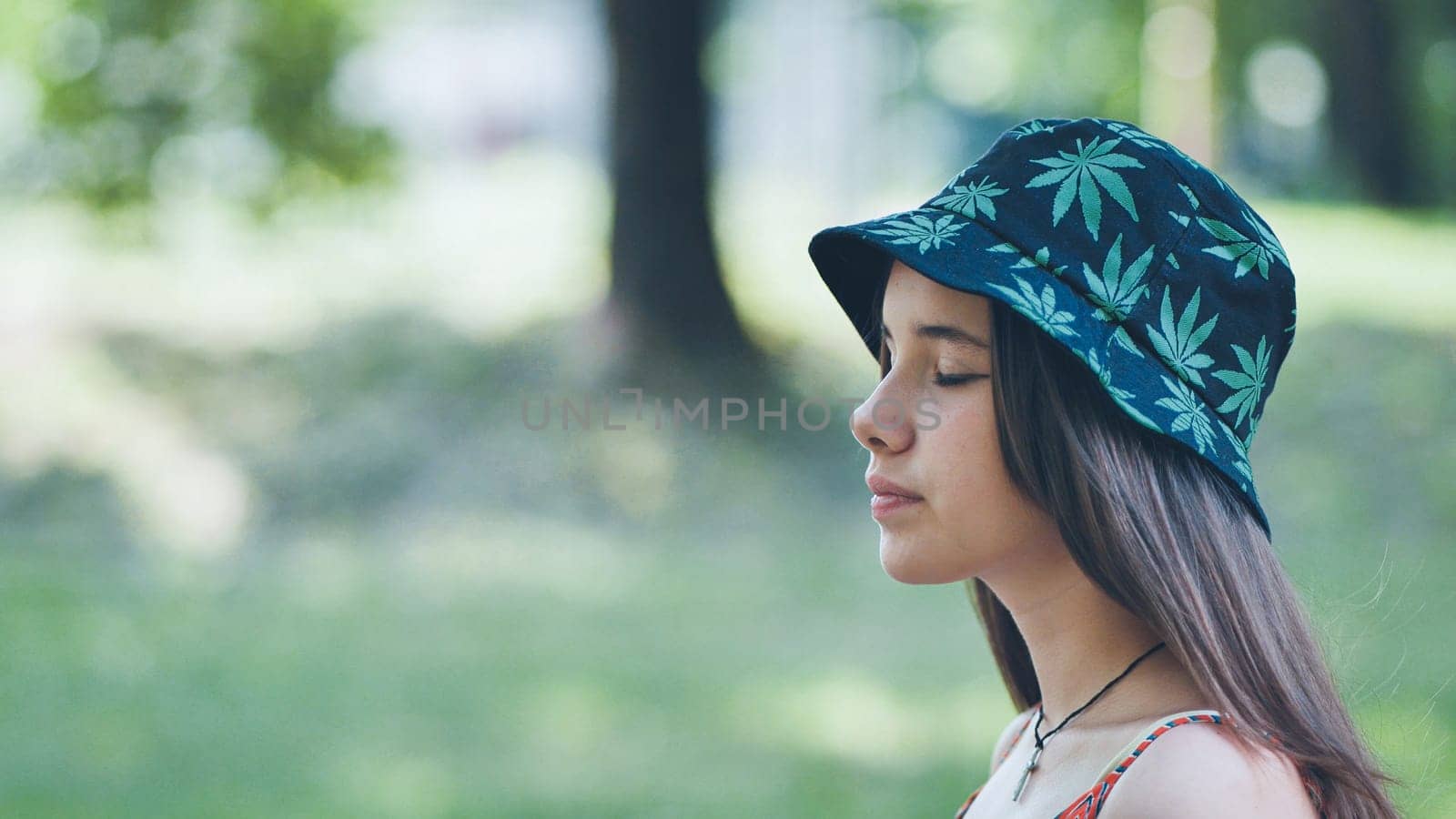 A teenage girl in a panama hat is walking through the park in the summer