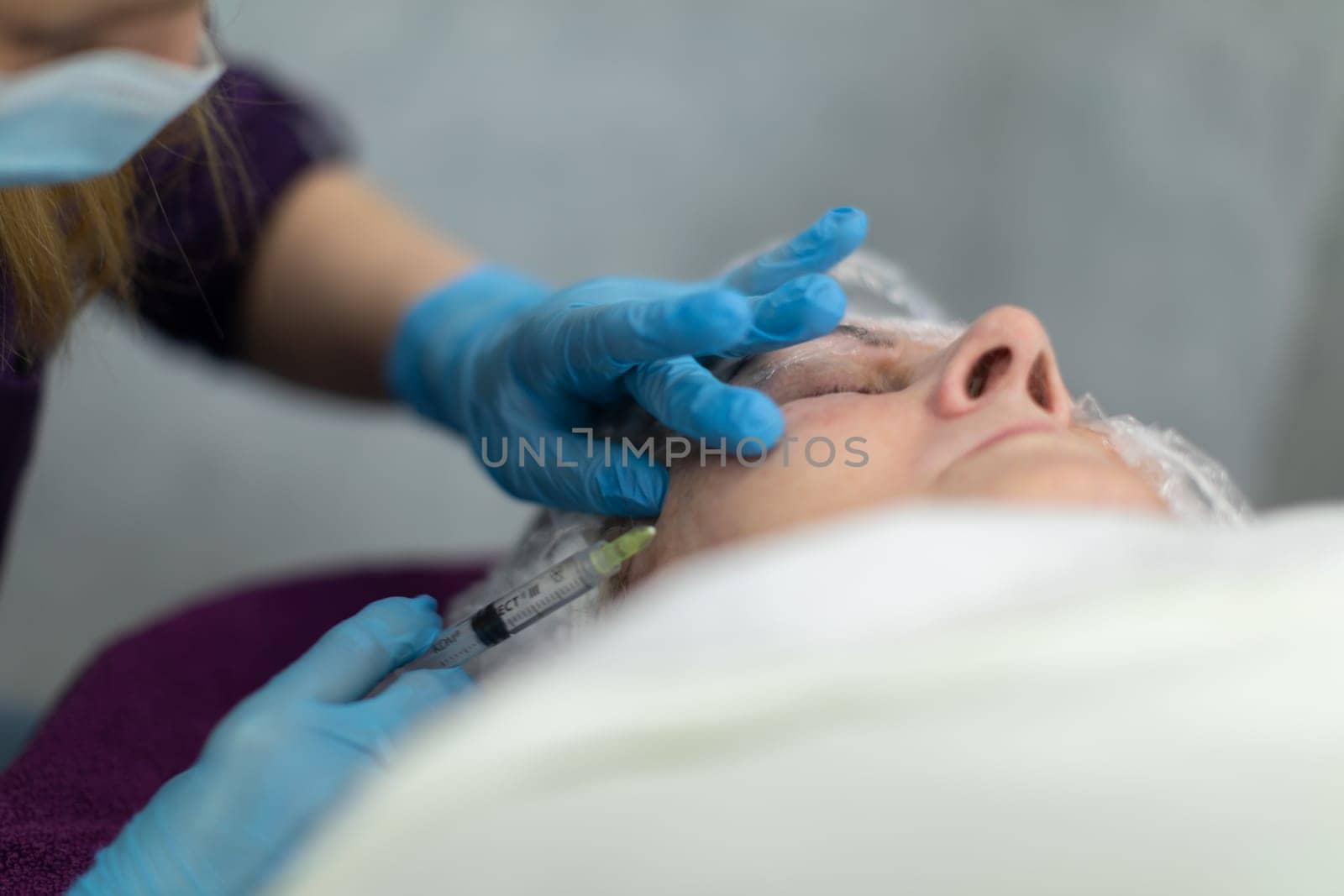 View from below of a female figure lying on a bed. A fragment of a white quilt can be seen in the foreground. The woman is lying in a beauty salon and experiencing beauty treatments.