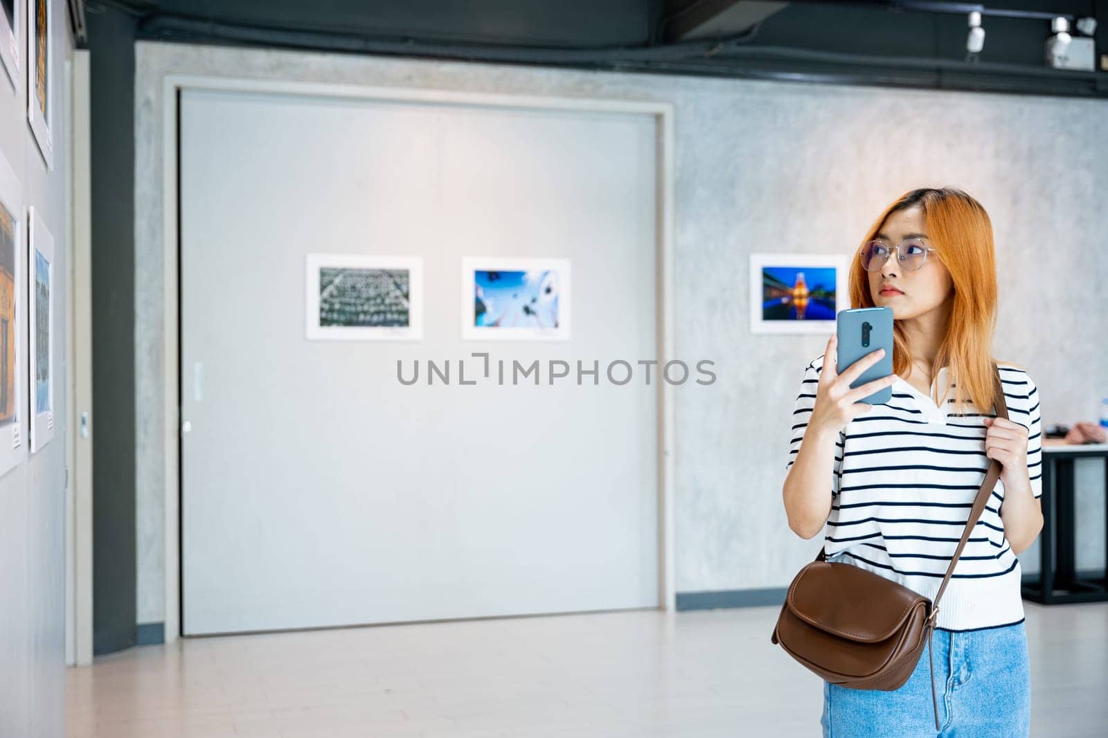 Visitor woman standing takes picture art gallery collection in front framed paintings pictures by Sorapop