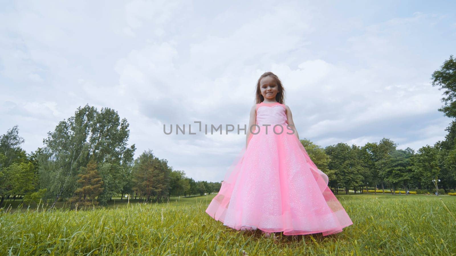 A girl in a pink princess dress is spinning in the park