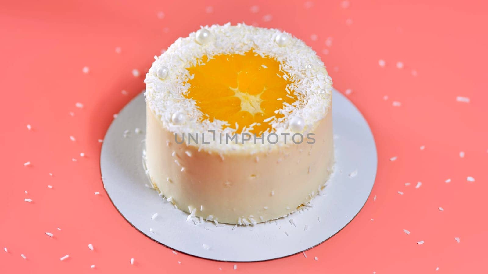Cake with orange and coconut shavings spun on a pink background