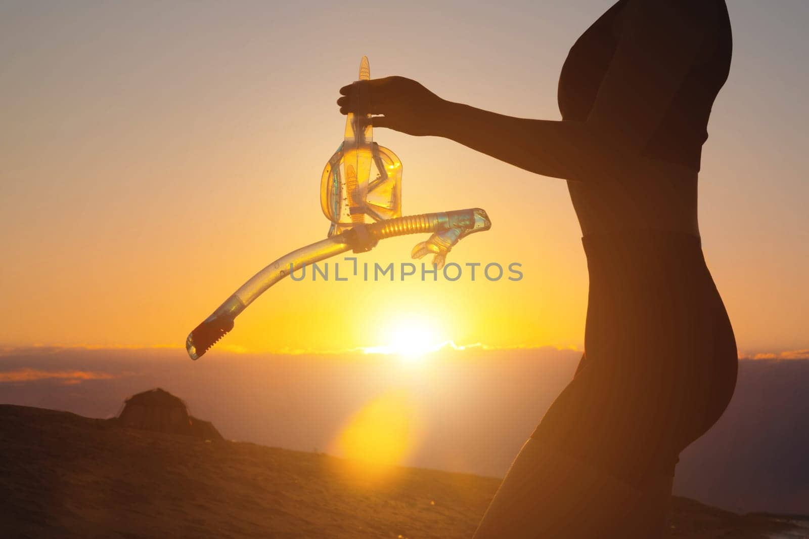 hand holds snorkeling goggles against the background of the sunset sky. Silhouette of a sexy woman holding scuba gear in her hands by yanik88