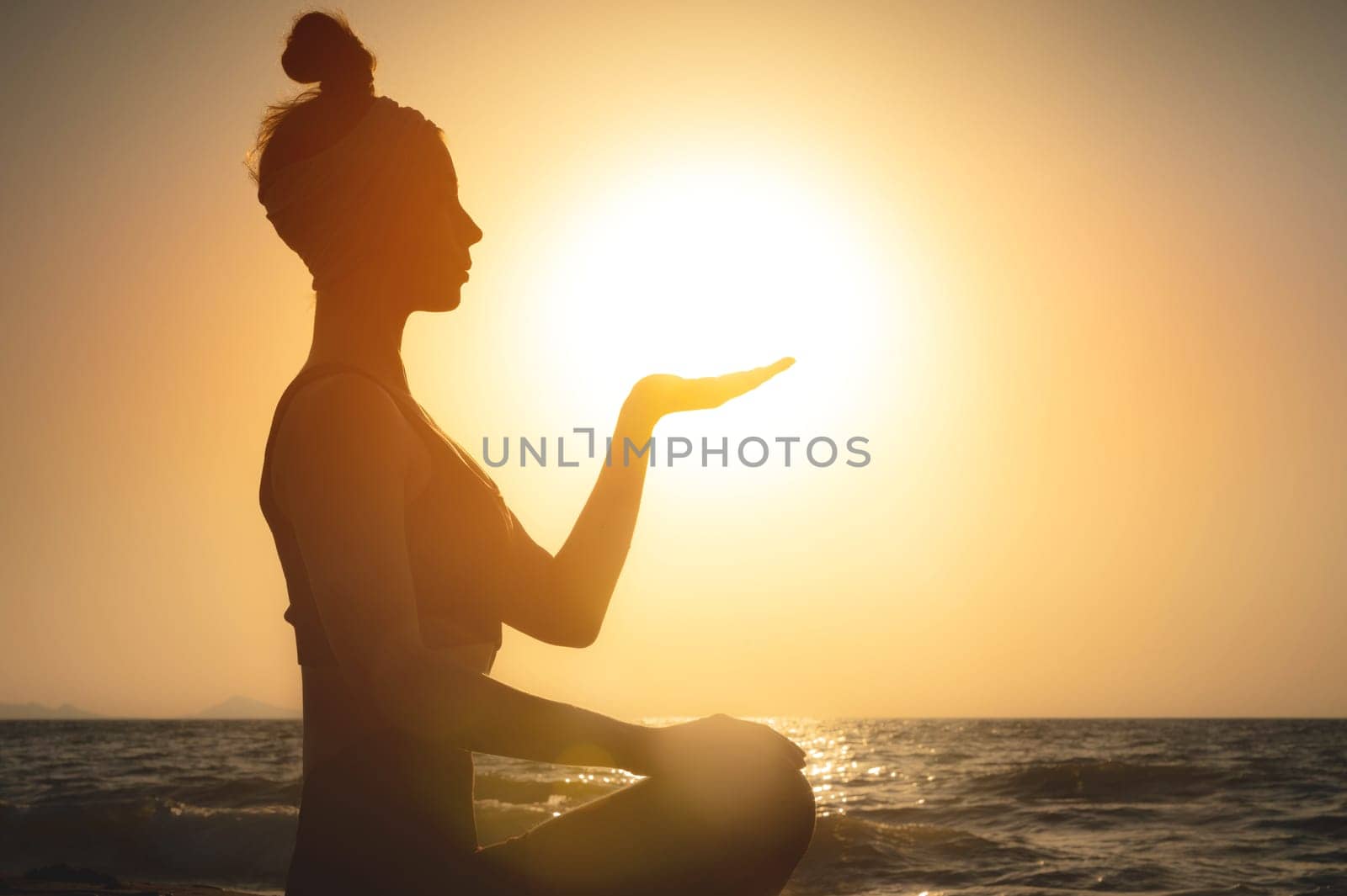 Portrait of a young woman in the form of a silhouette and hands holding the sun. Sunset over the sea, the sun on the palms of a calm girl.