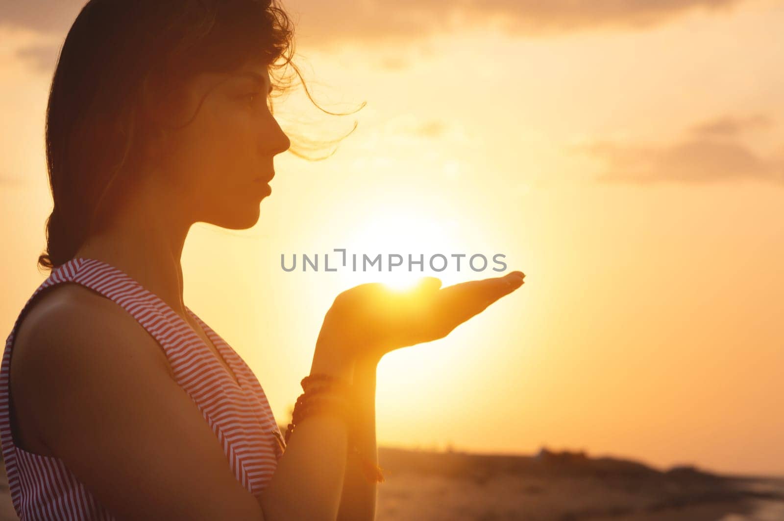 Portrait of a young woman in the form of a silhouette and hands holding the sun. Sunset over the sea, the sun on the palms of a calm girl by yanik88