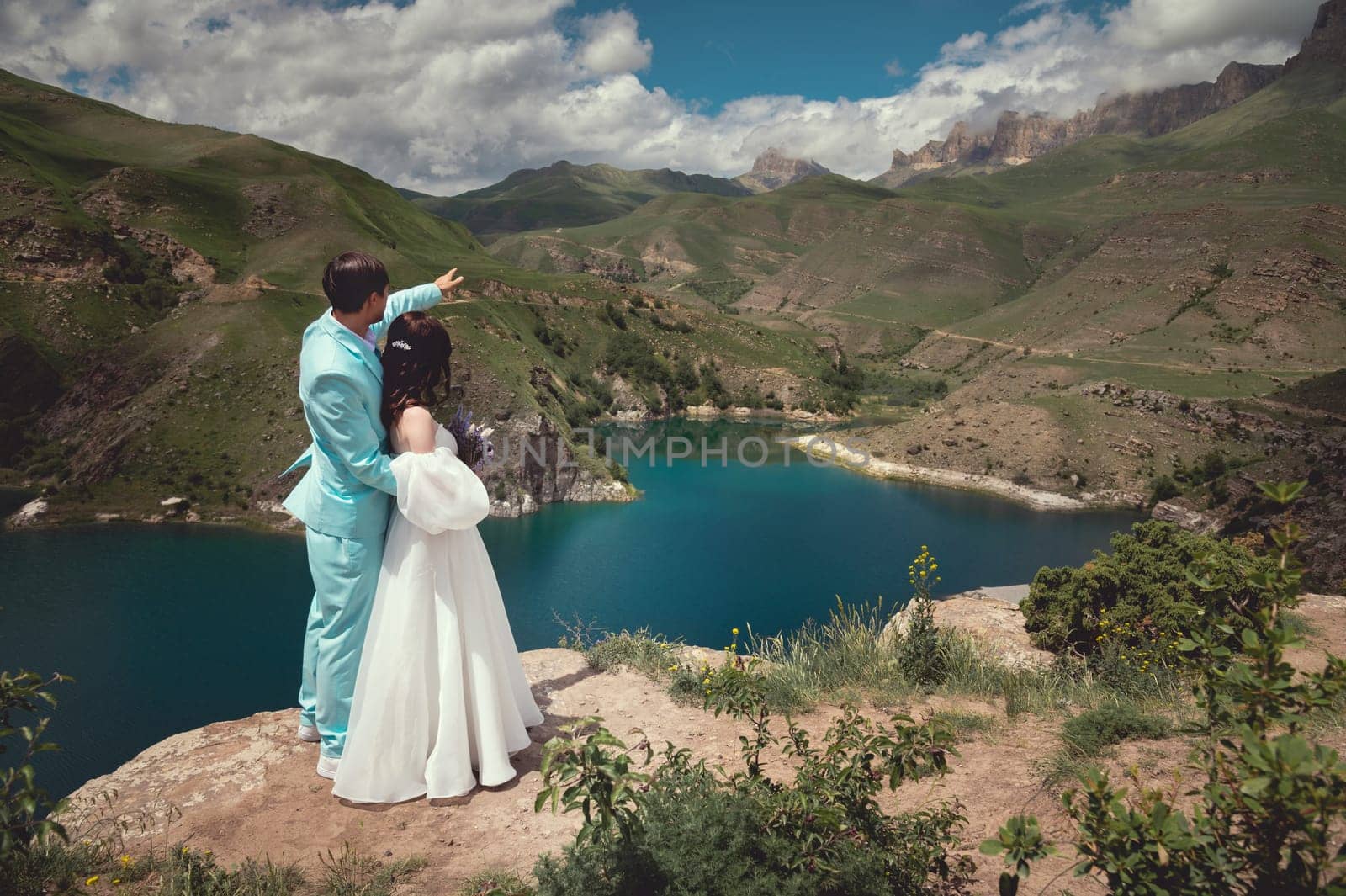 Love, wedding and married couple kissing by the lake outdoors in honor of their romantic marriage. Water, summer, mountains or a kiss by yanik88