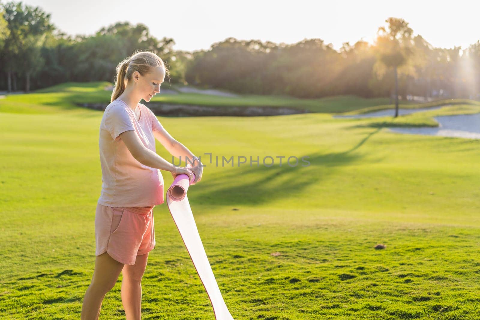 Energetic pregnant woman takes her workout outdoors, using an exercise mat for a refreshing and health-conscious outdoor exercise session.