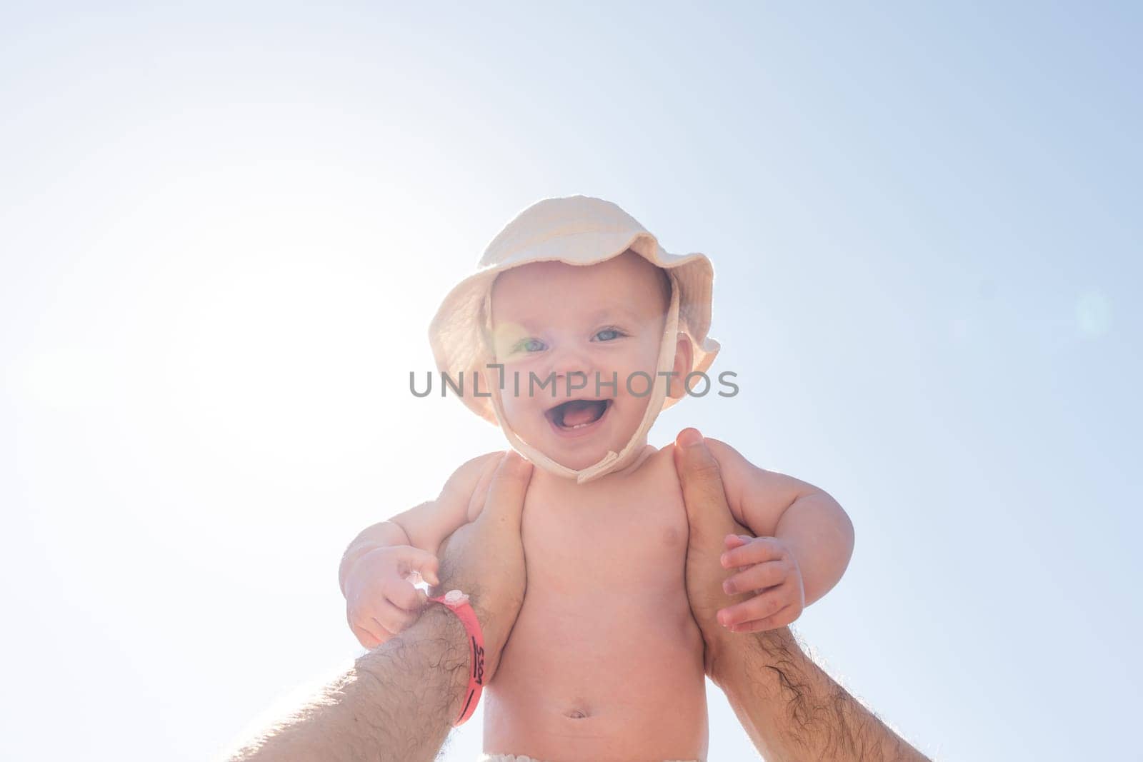 A father's hands securely holding his 6-month-old baby high, the sun's rays adding a magical touch. Concept of safety and nurturing in father-child relationships