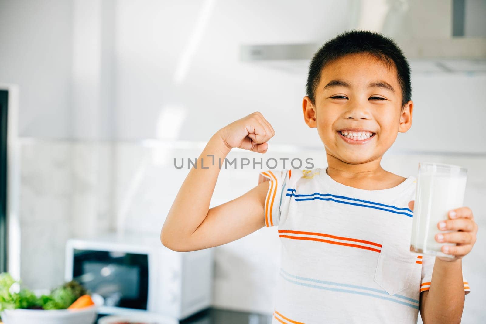 Asian little boy, cute son, holds milk in kitchen. Portrait of preschool child enjoying drink, smiling with joy. Happy kid sips calcium-rich liquid, radiating happiness at home give me.
