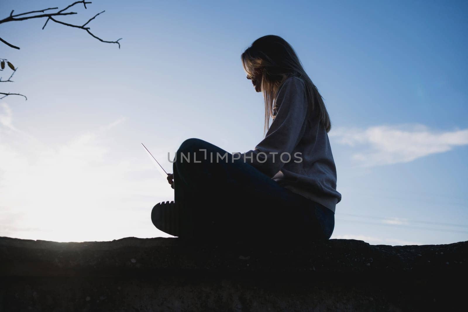 Woman freelancer uses laptop on cement wall outdoors against the sky. The woman to be focused on her work or enjoying some leisure time while using her laptop