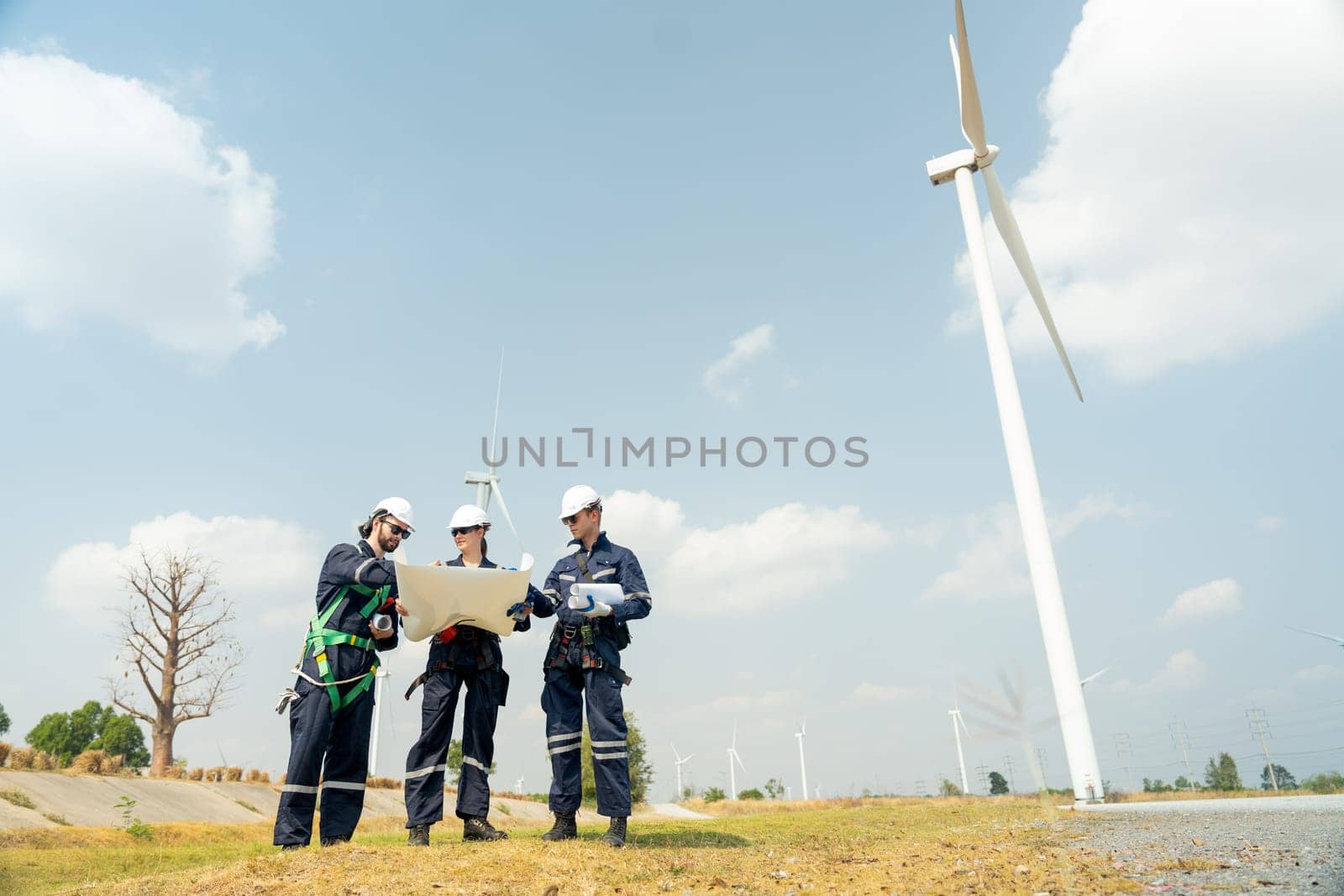 Group of professional technician workers stand with discuss the project in the paper plan and stand in front of wind turbine or windmill in area for power plant business. by nrradmin