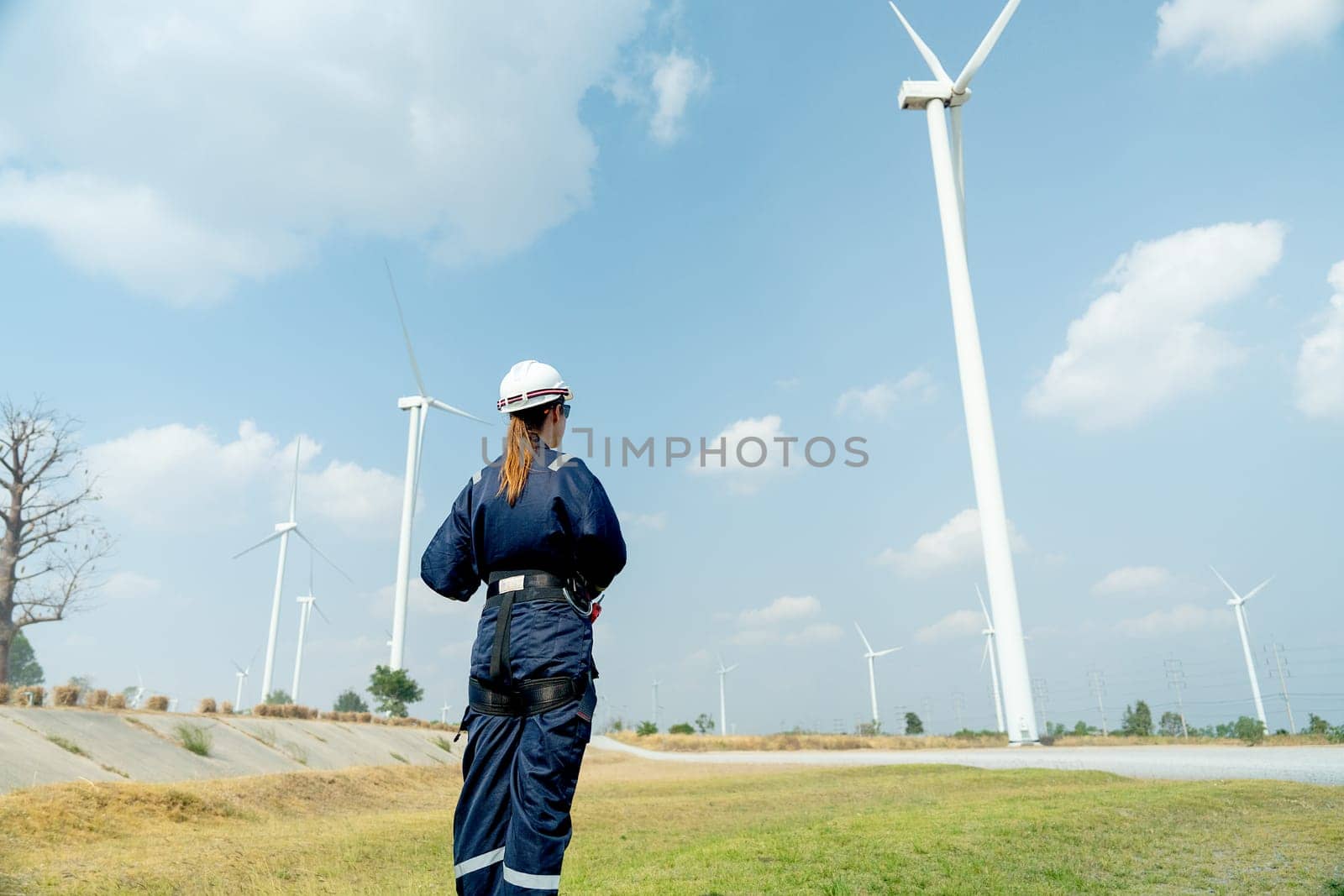 Back of professional technician woman worker stand in front of wind turbine or windmill in area for power plant business. by nrradmin