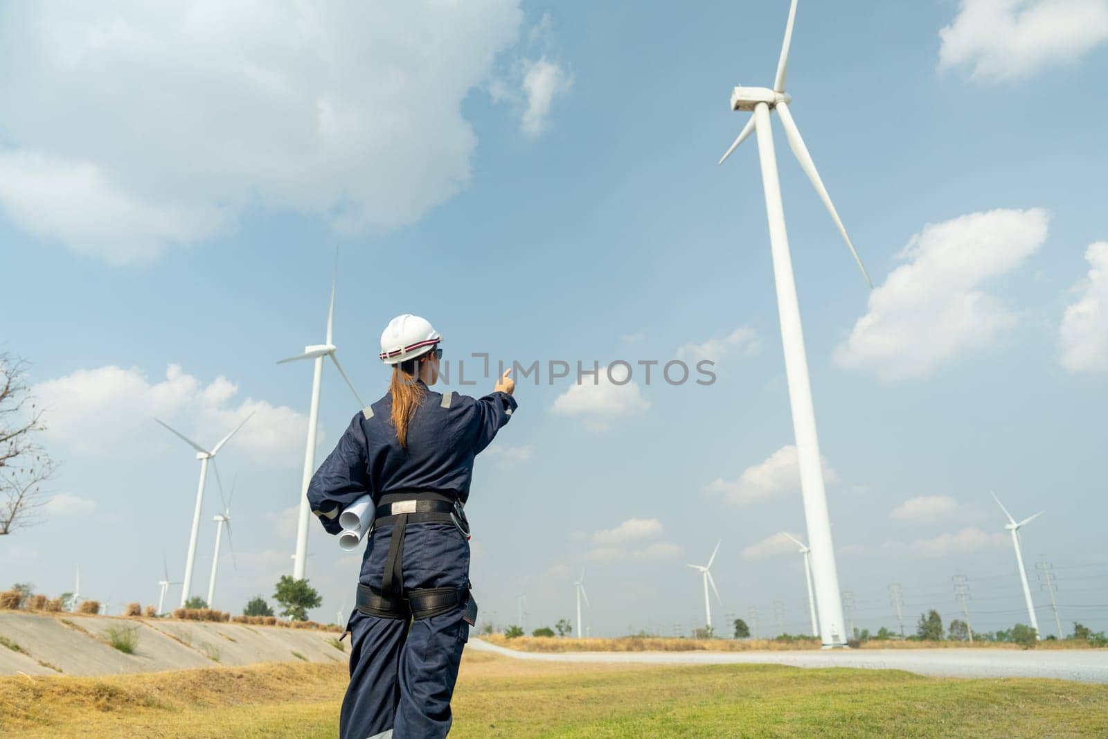 Professional technician woman worker stand in front of wind turbine or windmill and point to the pole in area for power plant business.