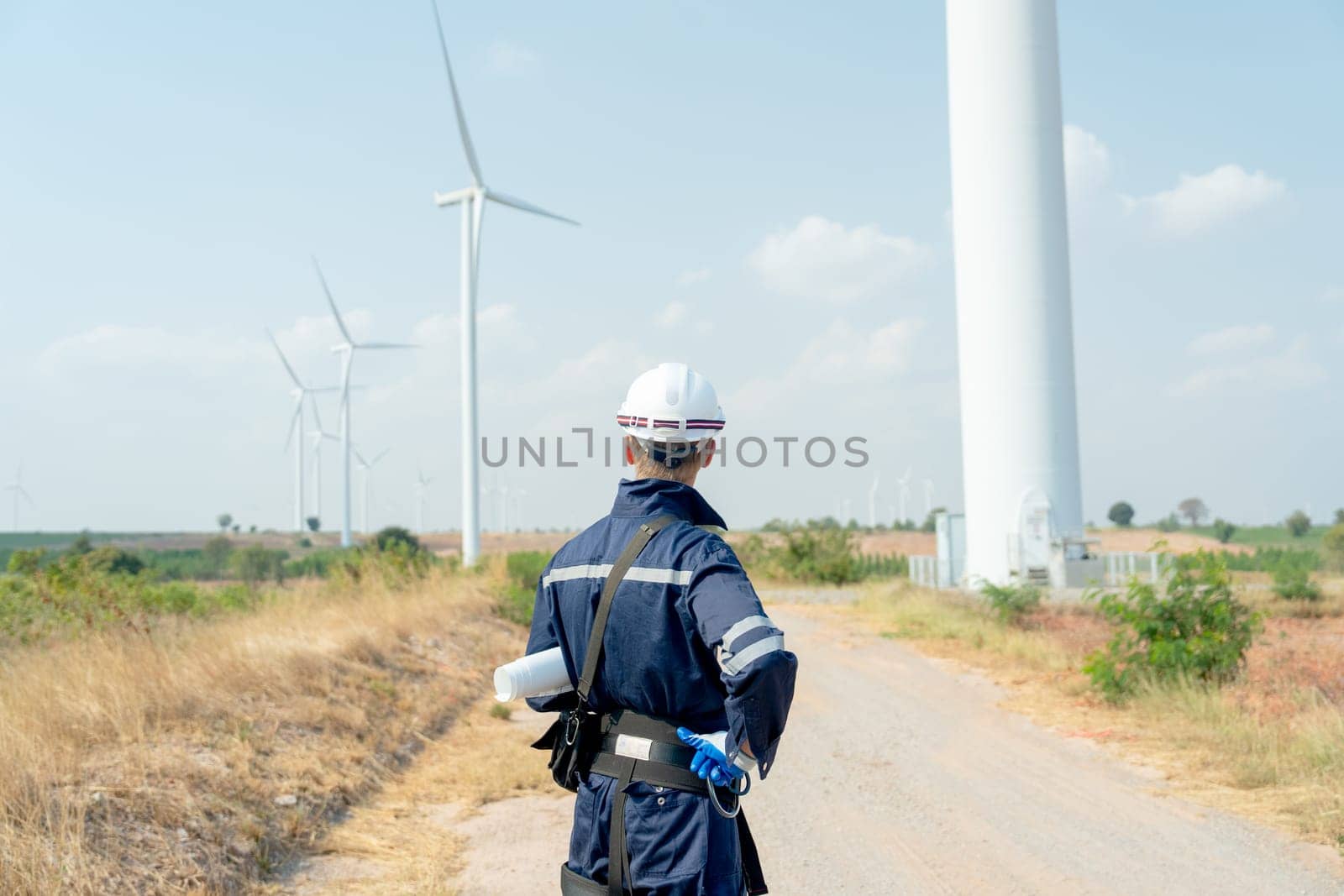 Back of technician worker man stand and look to wind turbine or windmill on the back in area of power plant business.