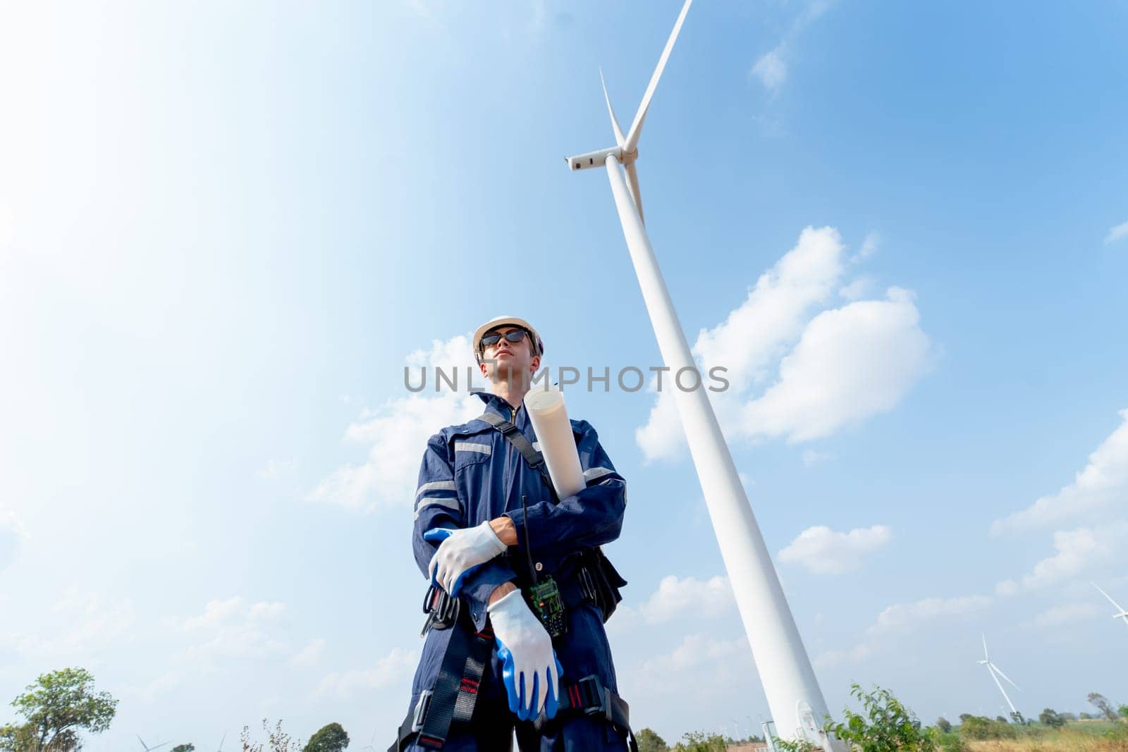 Lower view professional technician worker man stand in front of wind turbine or windmill with blue sky. by nrradmin