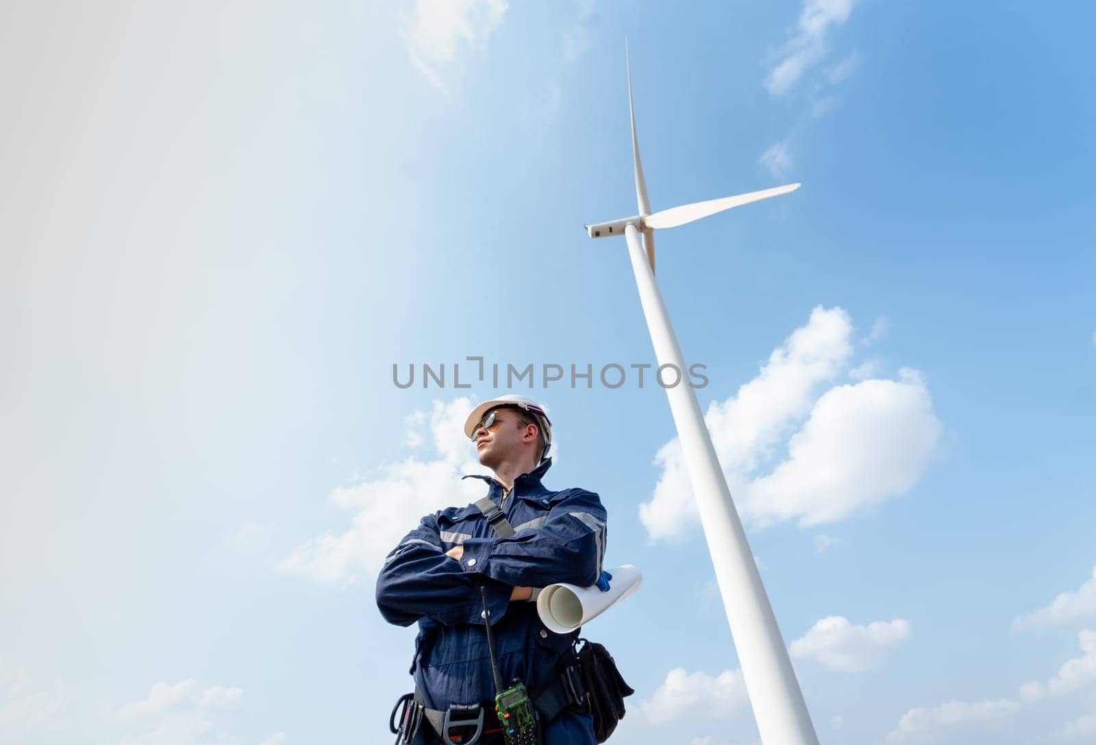 Professional technician worker man stand with arm-crossed also look to left side and stand in front of wind turbine or windmill with blue sky in concept of green energy for good environment. by nrradmin
