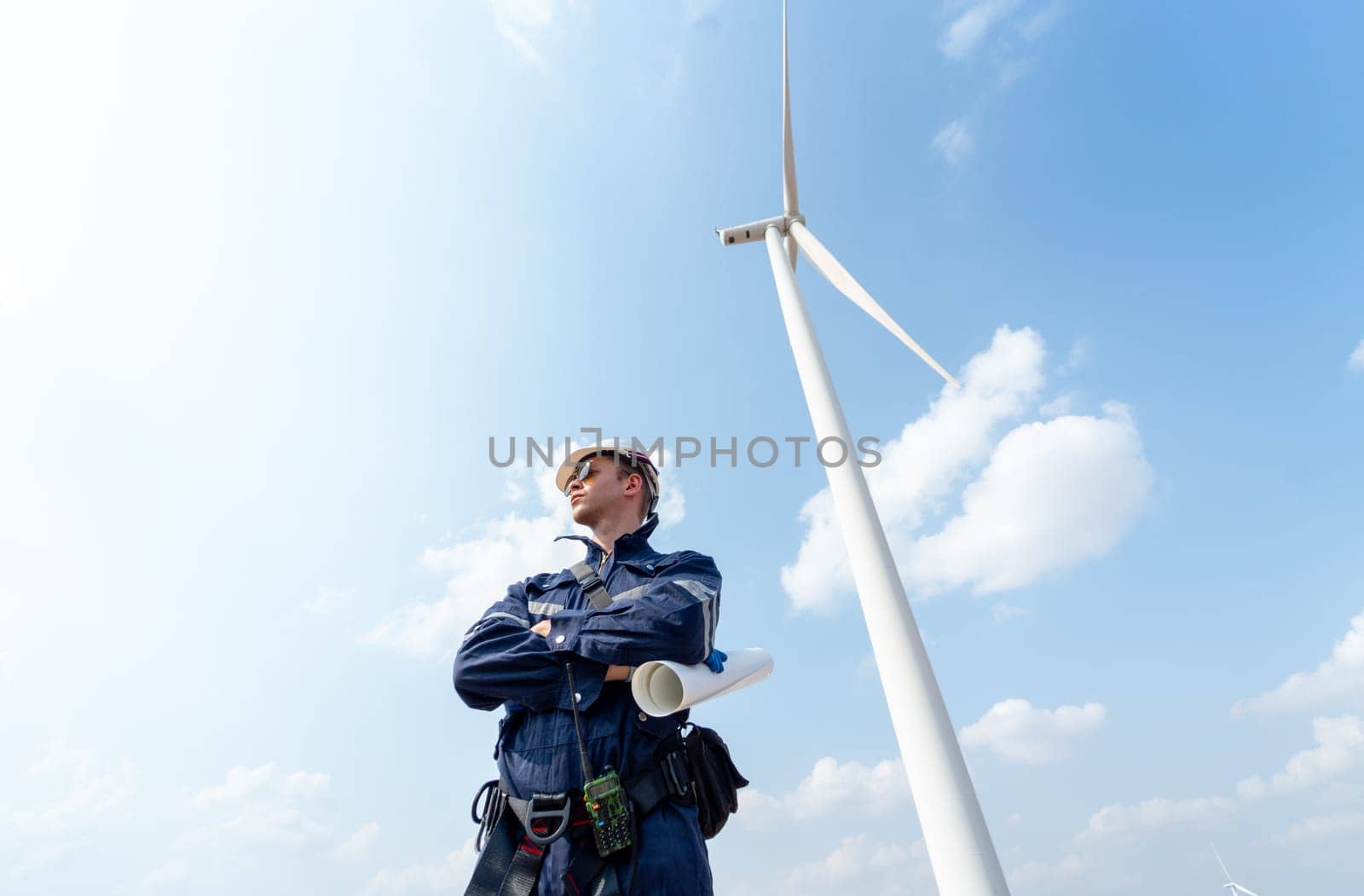 Professional technician worker man stand with arm-crossed and stand in front of wind turbine or windmill with blue sky in concept of green energy for good environment. by nrradmin