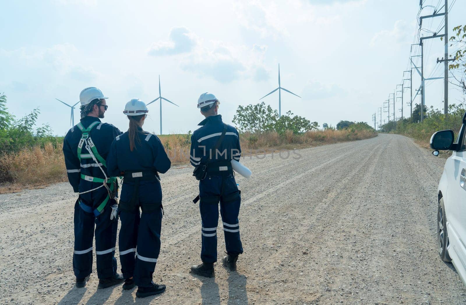 Back of group of technician workers stand on the road and discuss about work with windmill or wind turbine on the background.