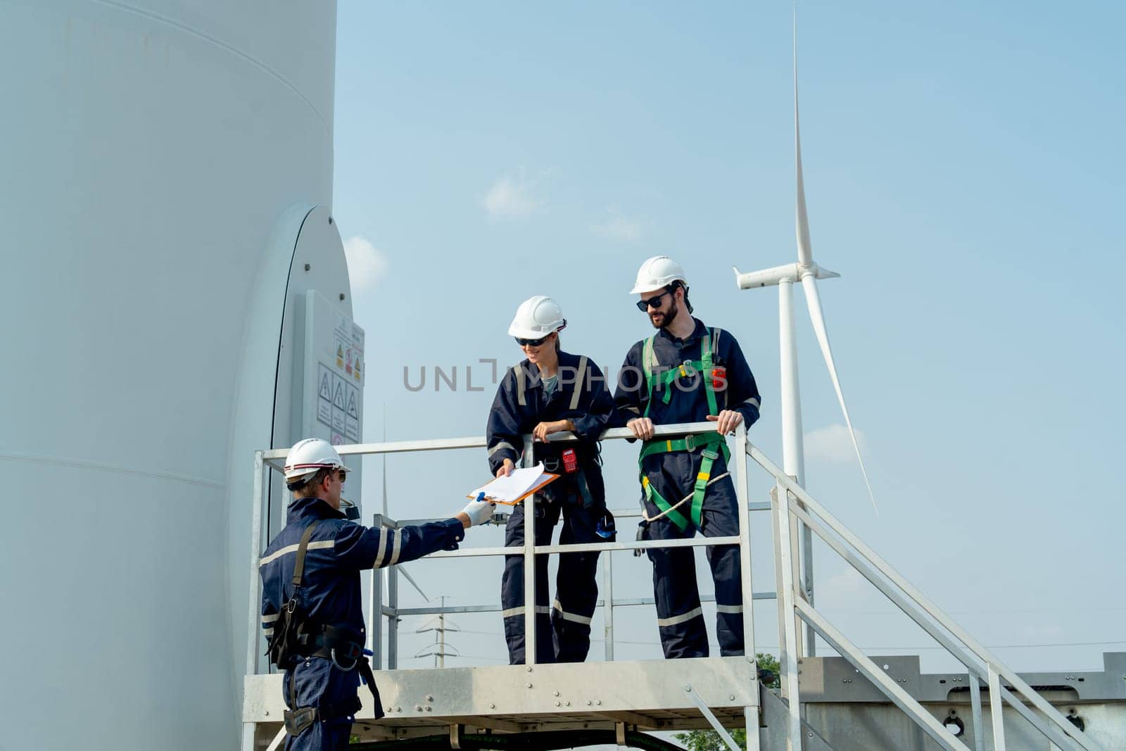 One of professional technican worker give the document to his coworker stand in base of windmill or wind turbine.