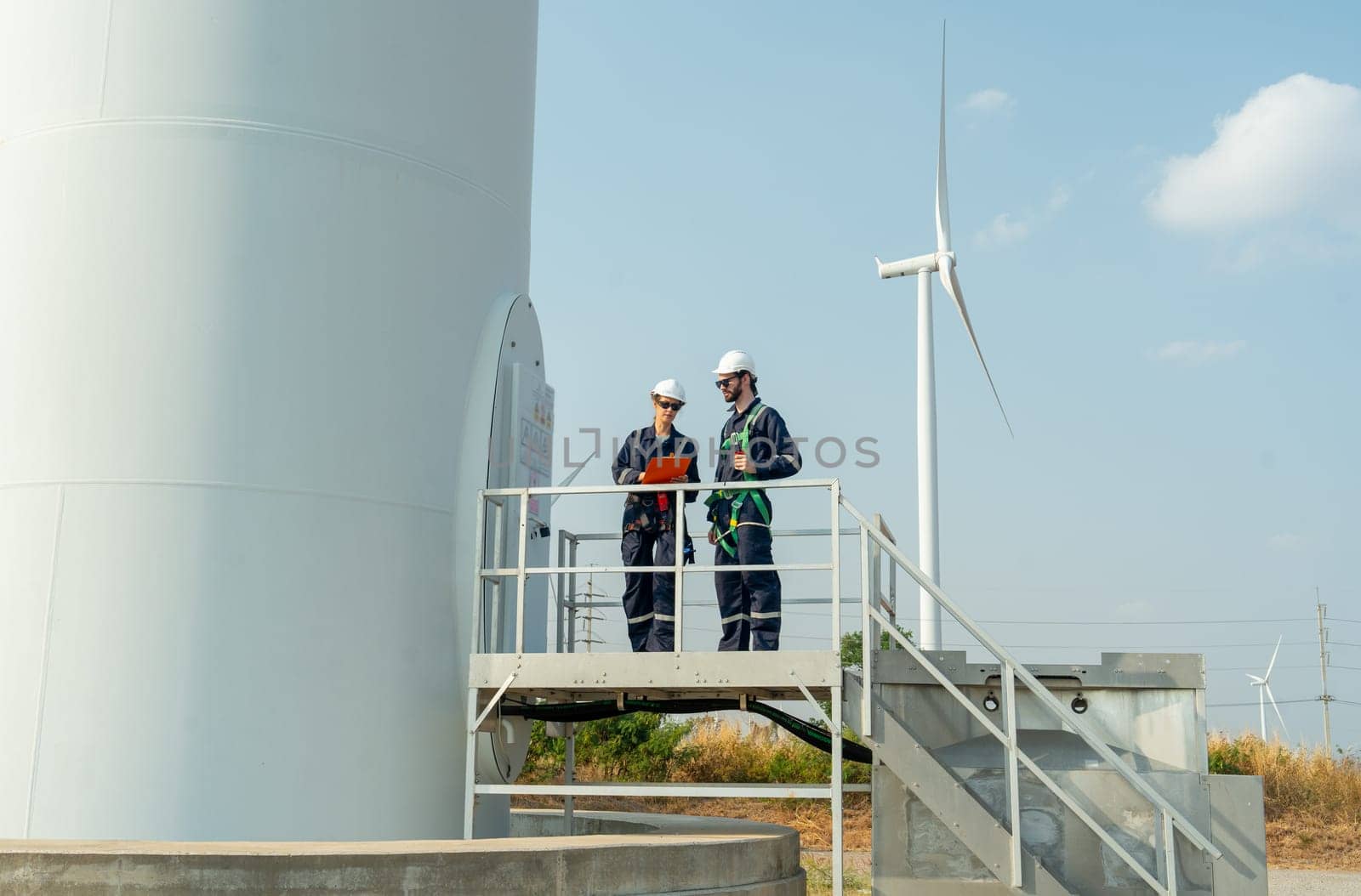 Wind shot two professional workers stand and discuss about work and stay in base of windmill or wind turbine in area of green power plant. by nrradmin