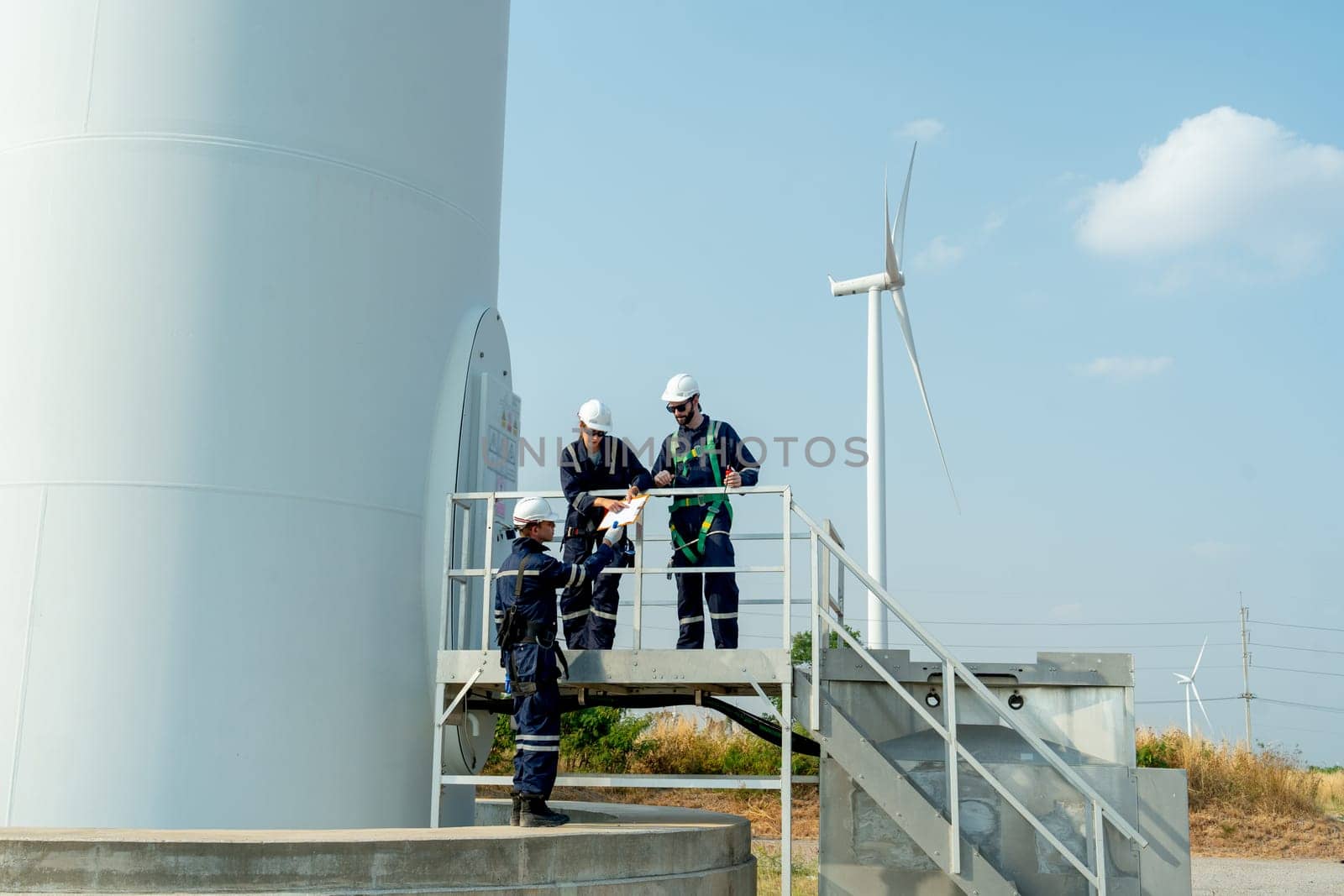 Wide shot of one professional technican worker give the document to his coworker stand in base of windmill or wind turbine.