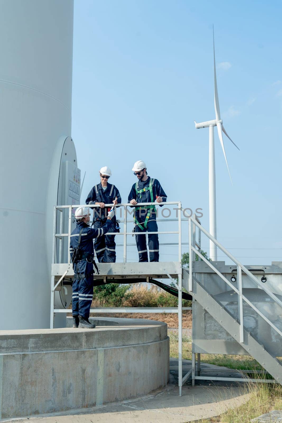 Vertical image one technican worker give the document to his coworker stand in base of windmill or wind turbine.