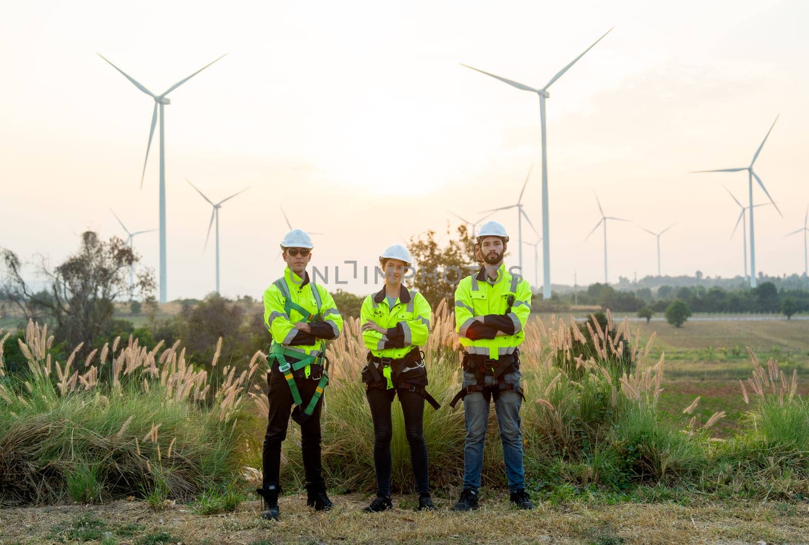 Group of technician workers stand with arm crossed and look at camera in front of windmill or wind turbine and evening light in area of power plant. by nrradmin