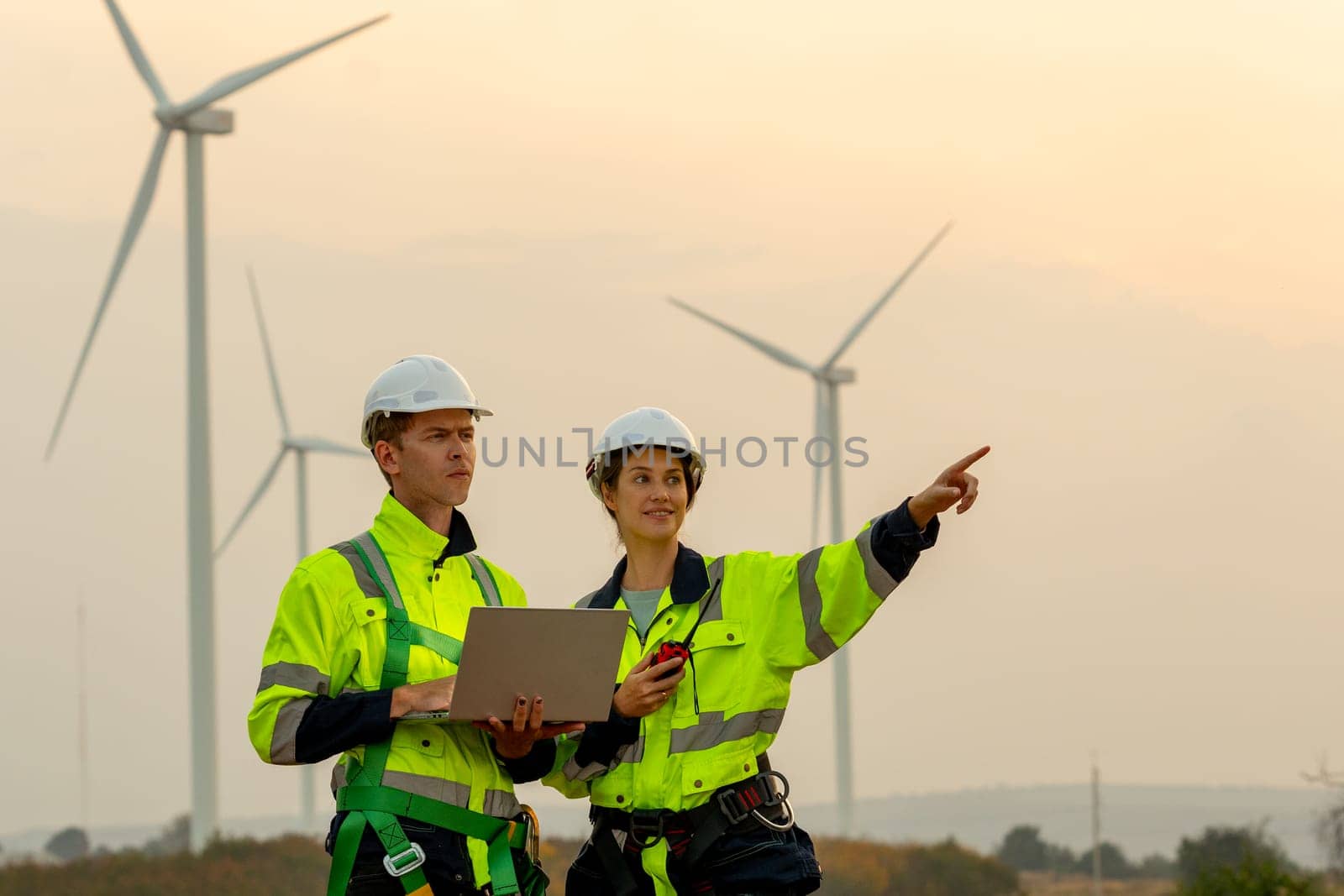 Portrait technician workers use laptop to work and stay with his co-worker point to right side in evening with windmill or wind turbine on the background. by nrradmin