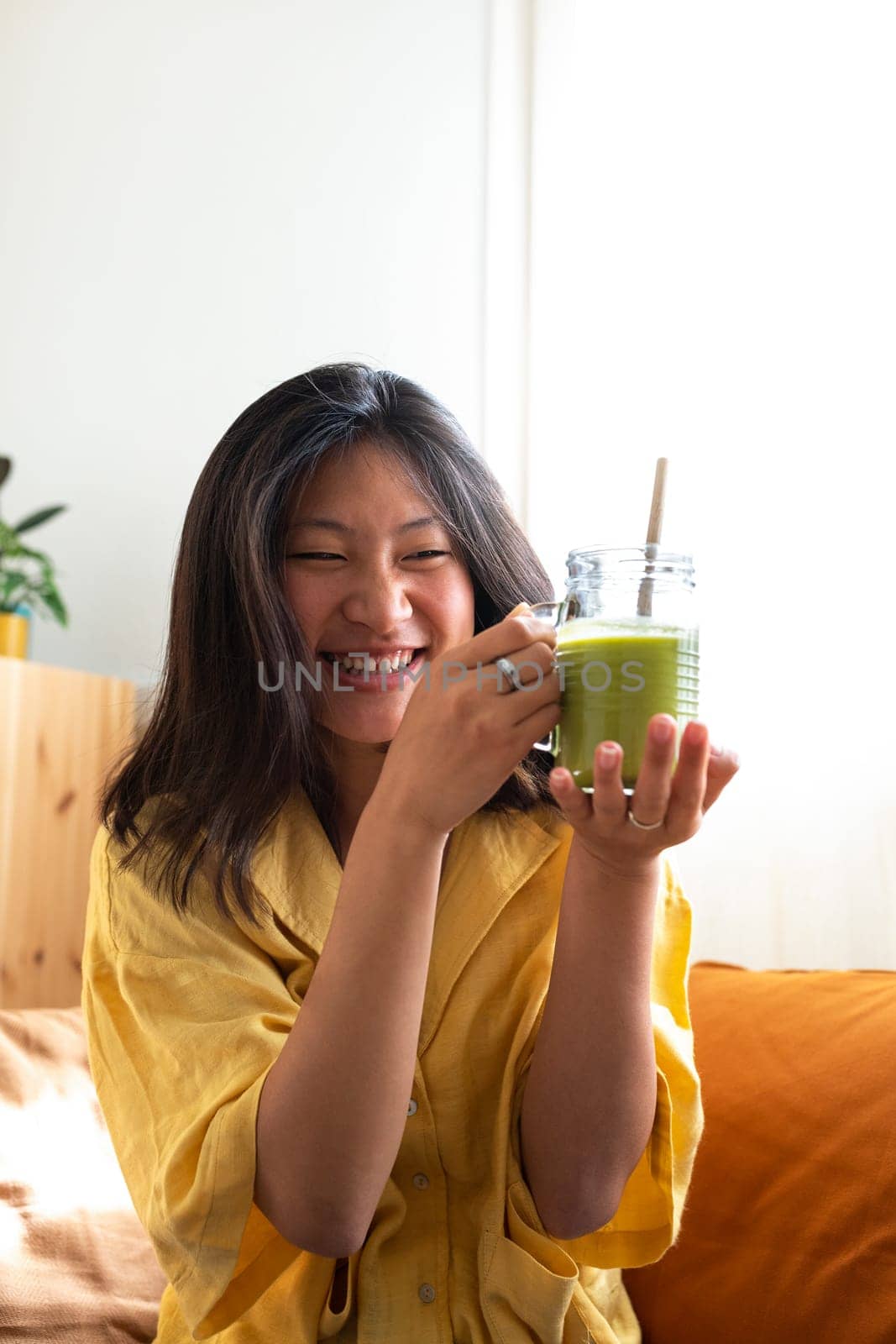 Happy teen asian girl showing healthy green juice. Vertical image. Healthy lifestyle concept.