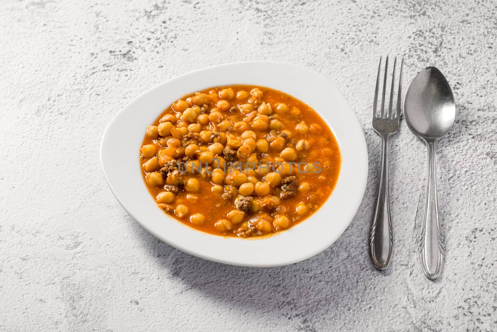 Chickpea stew with minced meat on a white porcelain plate on a stone table