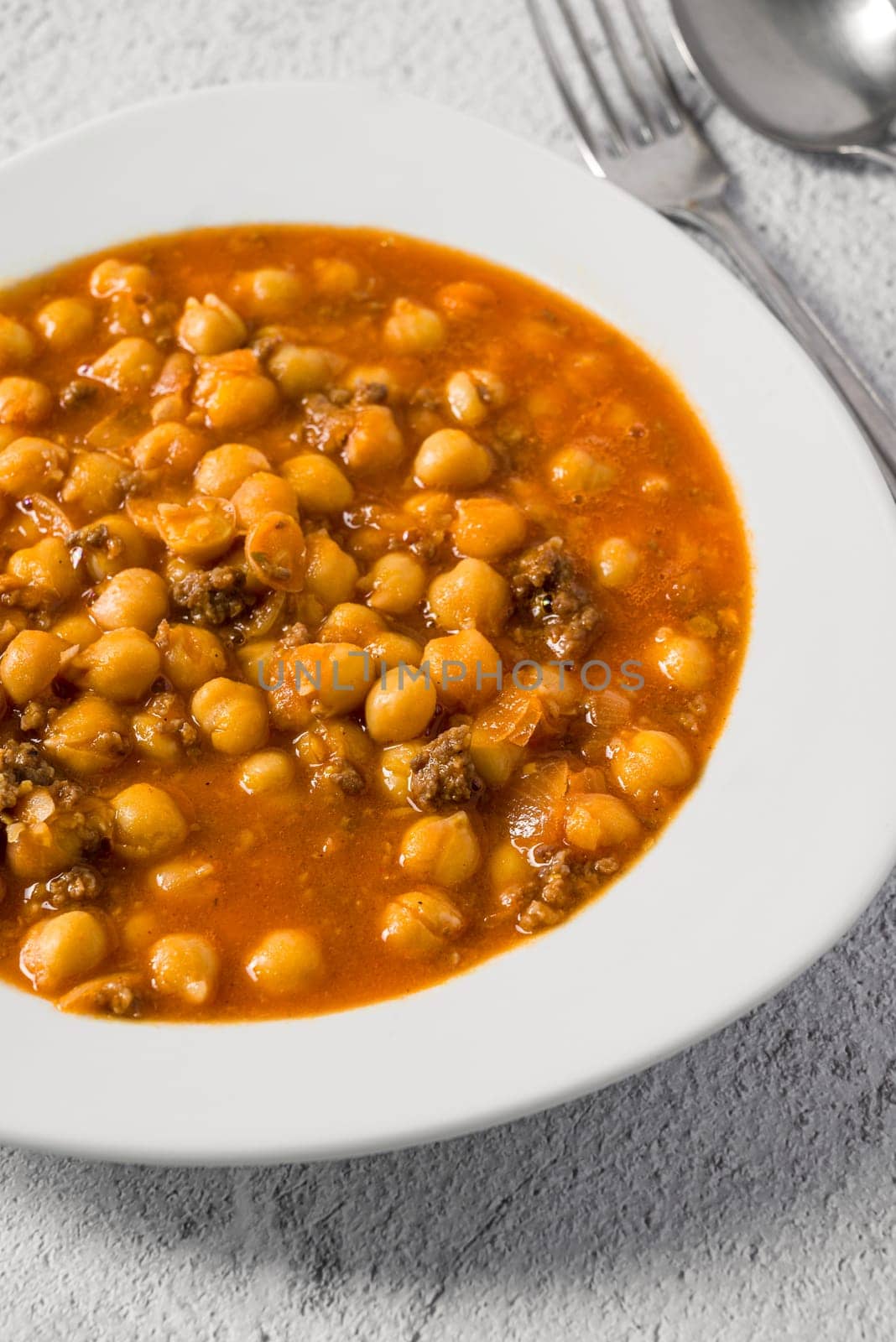 Chickpea stew with minced meat on a white porcelain plate on a stone table by Sonat