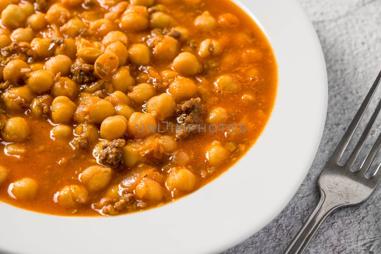 Chickpea stew with minced meat on a white porcelain plate on a stone table by Sonat