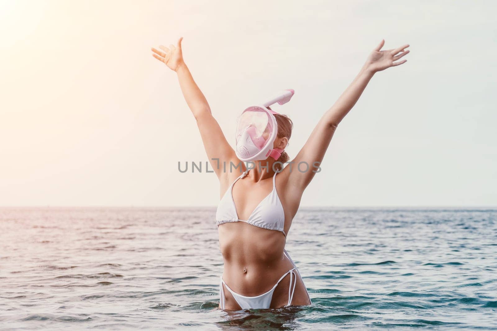 Young happy woman in white bikini and wearing pink mask gets ready for sea snorkeling. Positive smiling woman relaxing and enjoying water activities with family summer travel holidays vacation on sea. by panophotograph