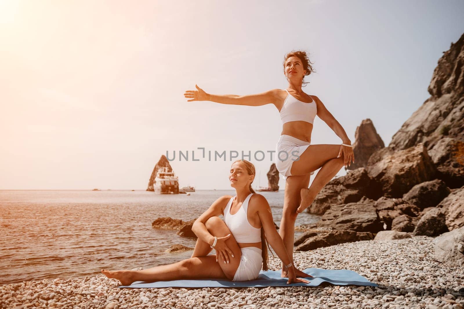 Woman sea yoga. Two happy women practicing yoga on the beach with ocean and rock mountains. Motivation and inspirational fit and exercising. Healthy lifestyle outdoors in nature, fitness concept. by panophotograph