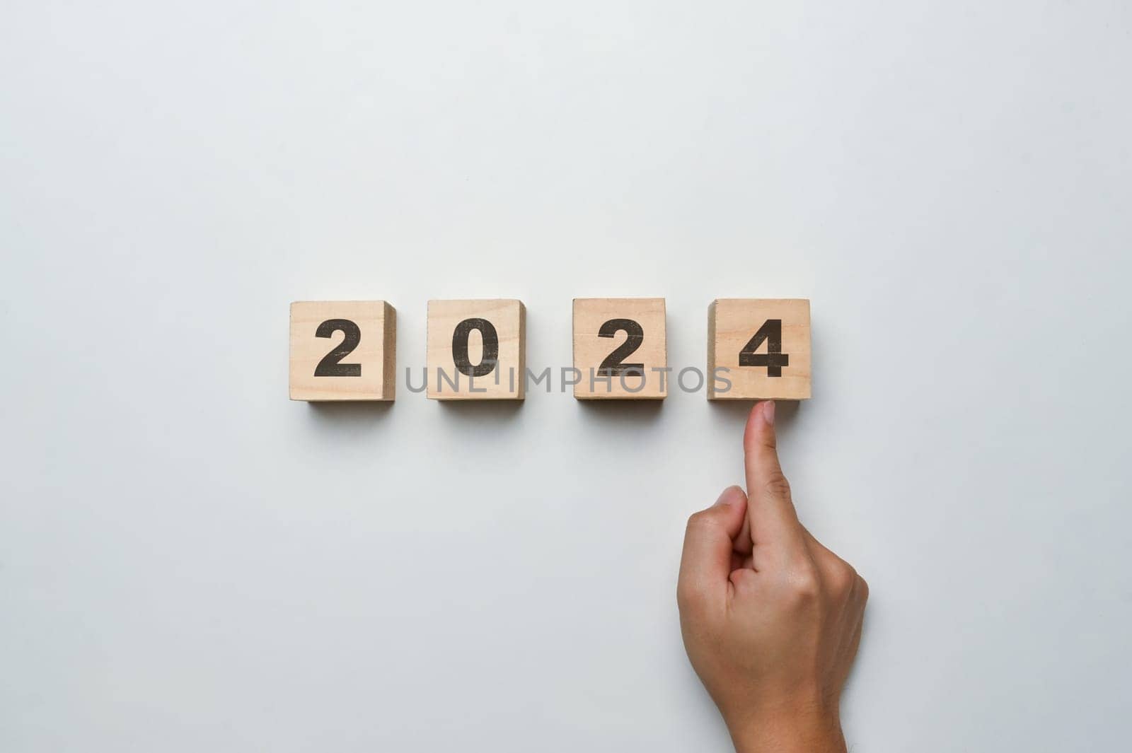 Hand pointing Wooden cube blocks with 2024 text on white background. Start new year and business vision concept.