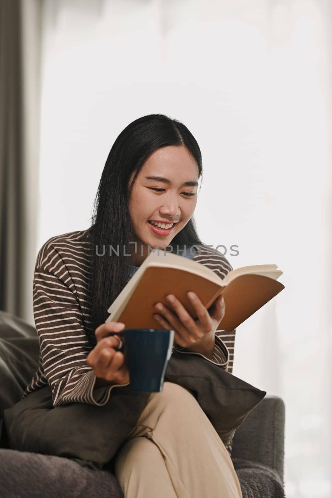 Relaxed young woman in casual clothes reading book, spending free time at home on weekend by prathanchorruangsak