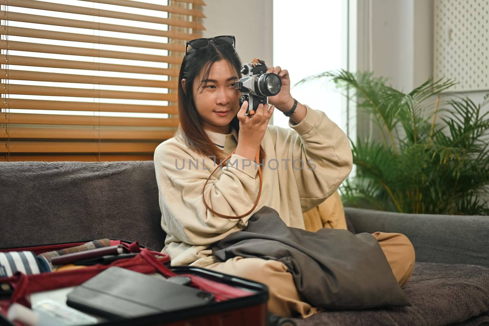 Young woman with clothes in suitcase sitting on couch, preparing for vacations trip.