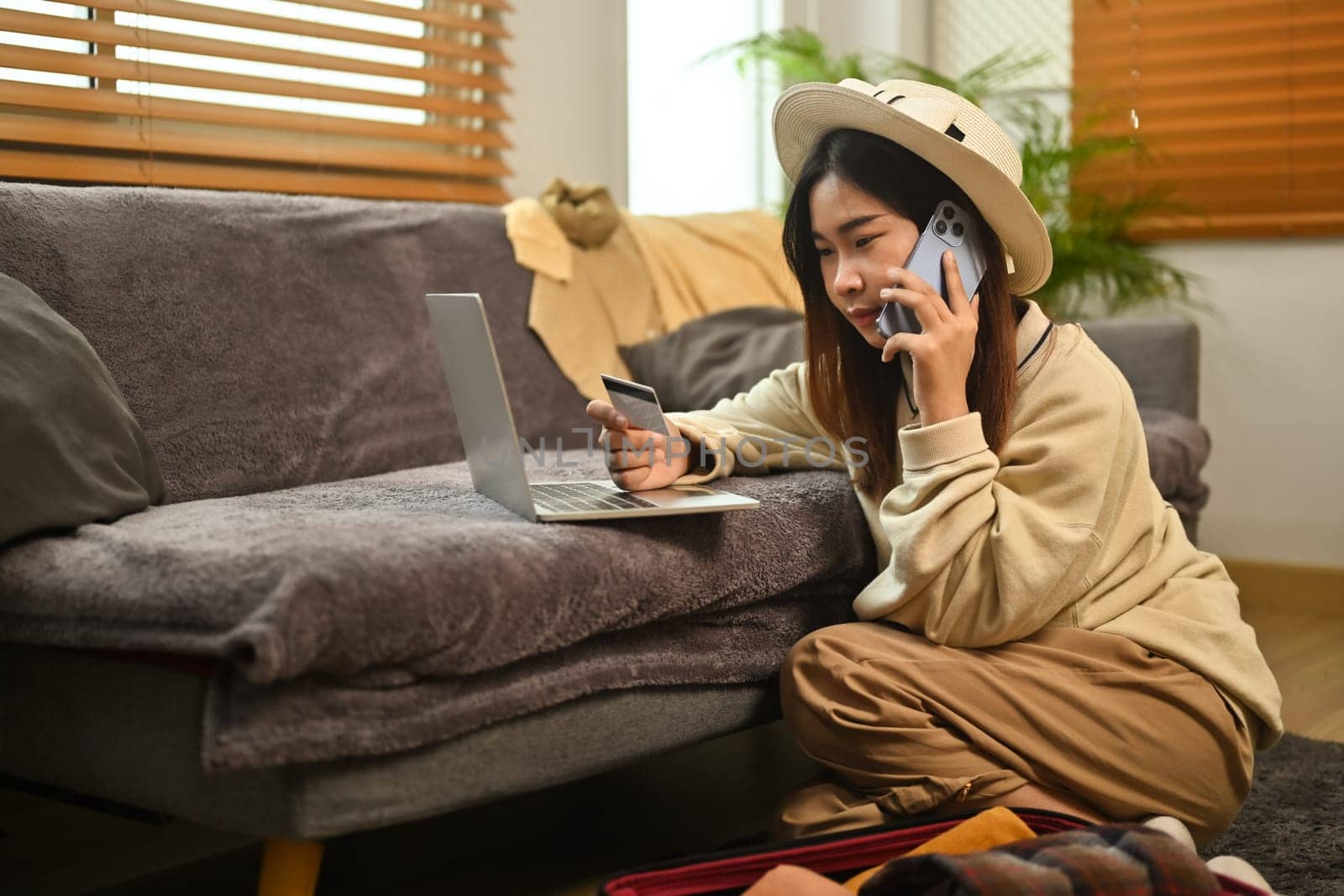 Young woman talking on mobile phone and making an online hotel reservation on laptop.