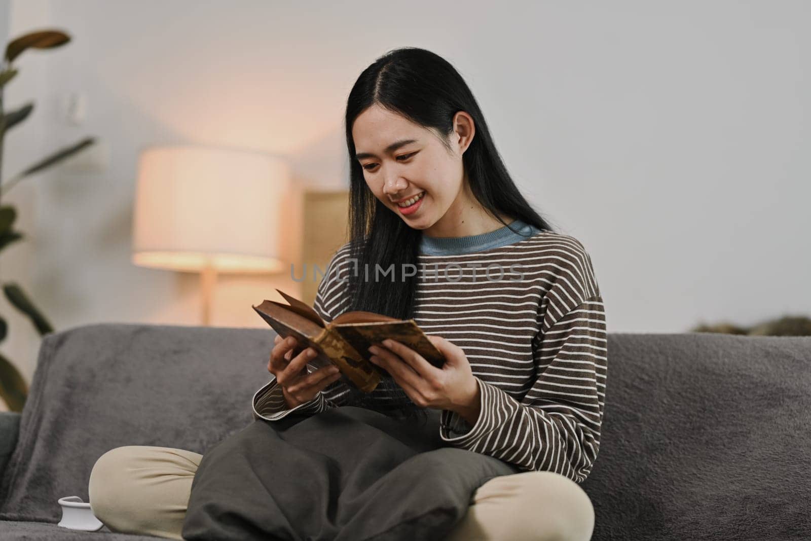 Beautiful young woman sitting on cozy sofa and reading book. People, leisure and lifestyle concept.