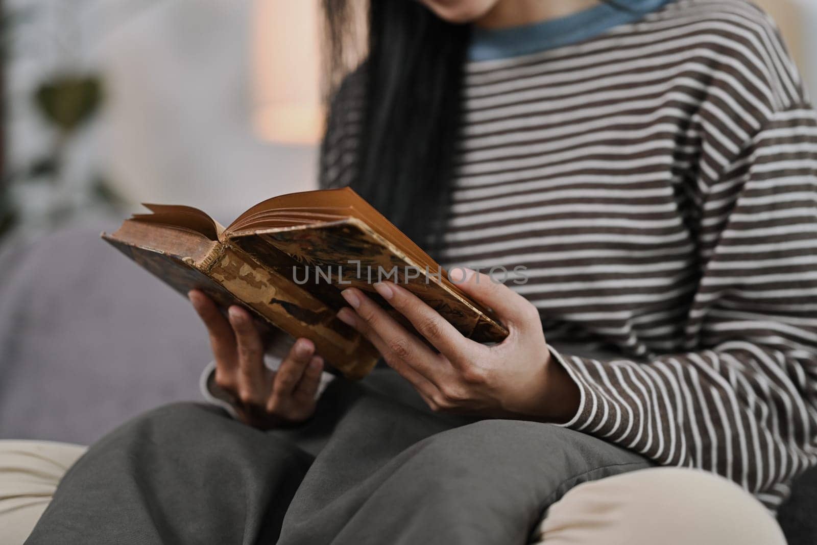 Calm young woman reading book on couch at home. People, leisure and lifestyle concept.